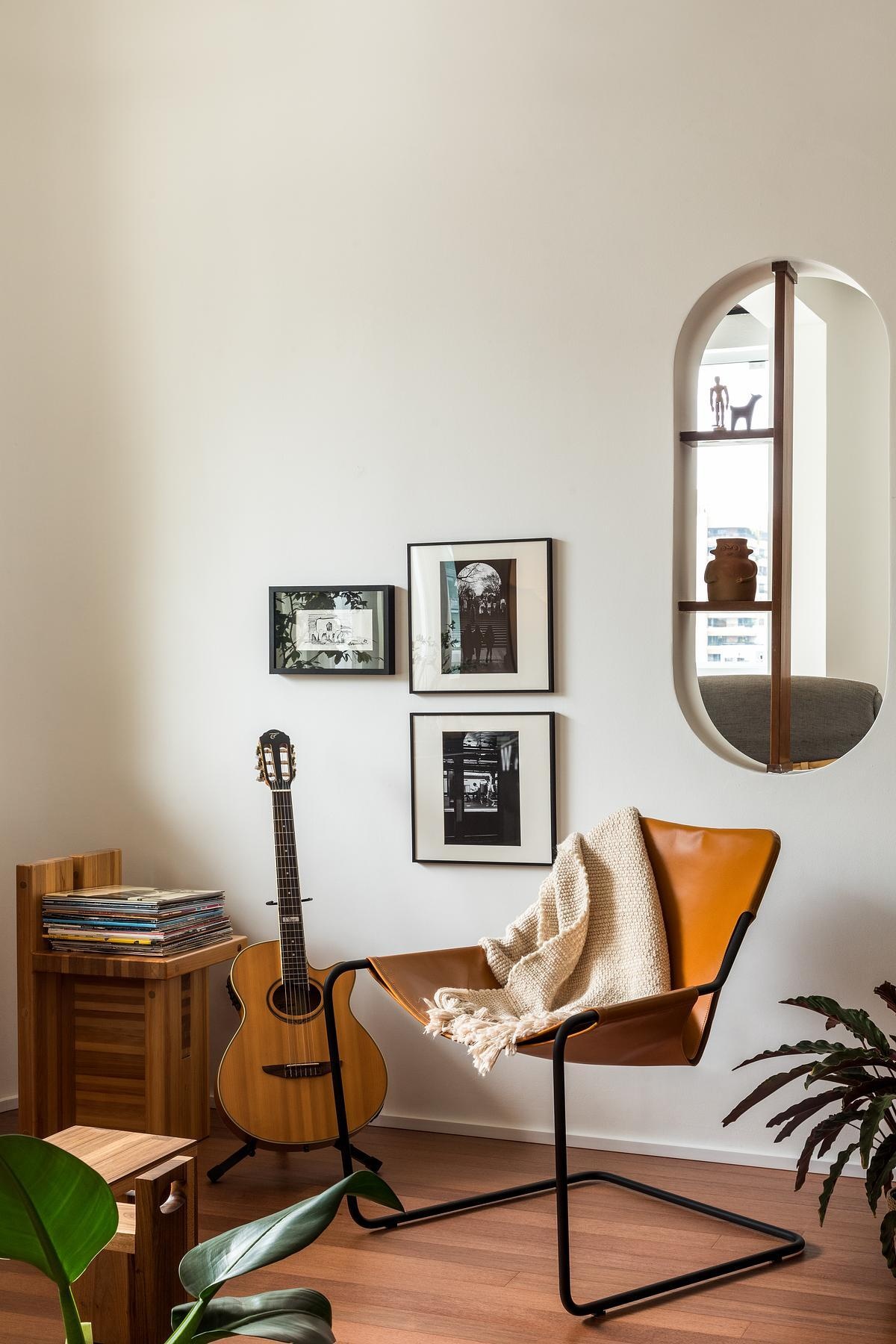 In a sitting area by a curved window, Brazilian design takes center stage. It centers on the Bag Armchair by Sérgio Rodrigues. Here, the chair sits near a Jabuticaba tree, creating a grounded, contemplative space. Personal photography, wood cabinetry, and a mix of Brazilian seating give it an intimate, collected atmosphere.