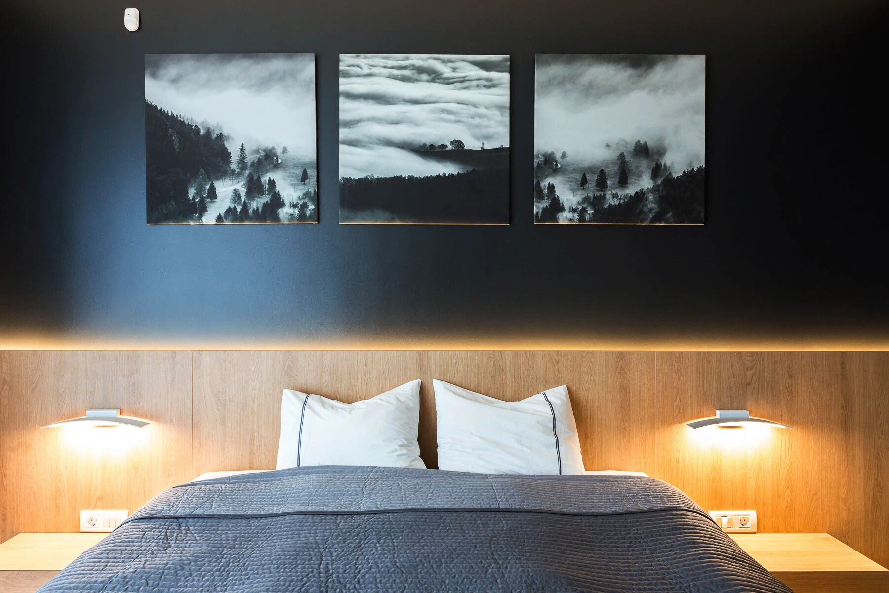 El acogedor dormitorio cuenta con una pared negra, una cabecera de madera y una iluminación ambiental suave, que combina la calma escandinava con la elegancia moderna.