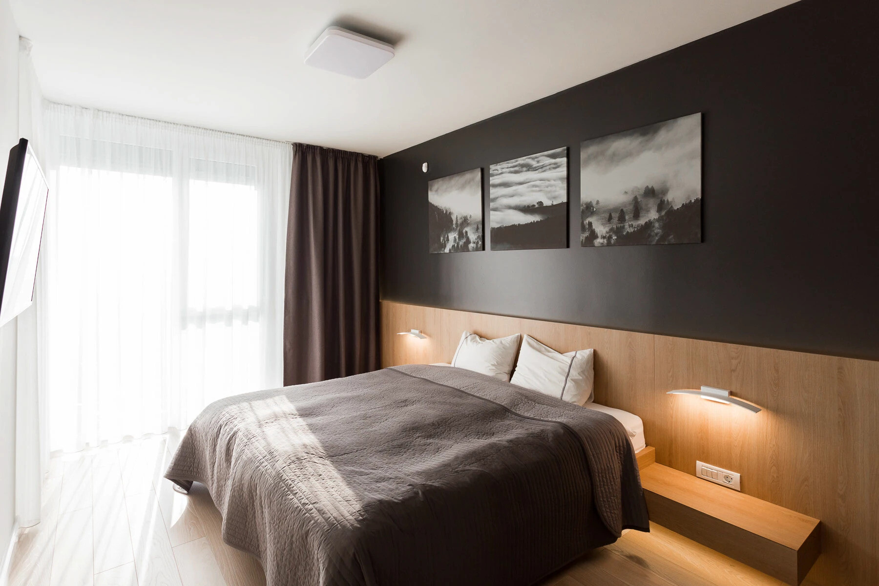 El acogedor dormitorio cuenta con una pared negra, una cabecera de madera y una iluminación ambiental suave, que combina la calma escandinava con la elegancia moderna.