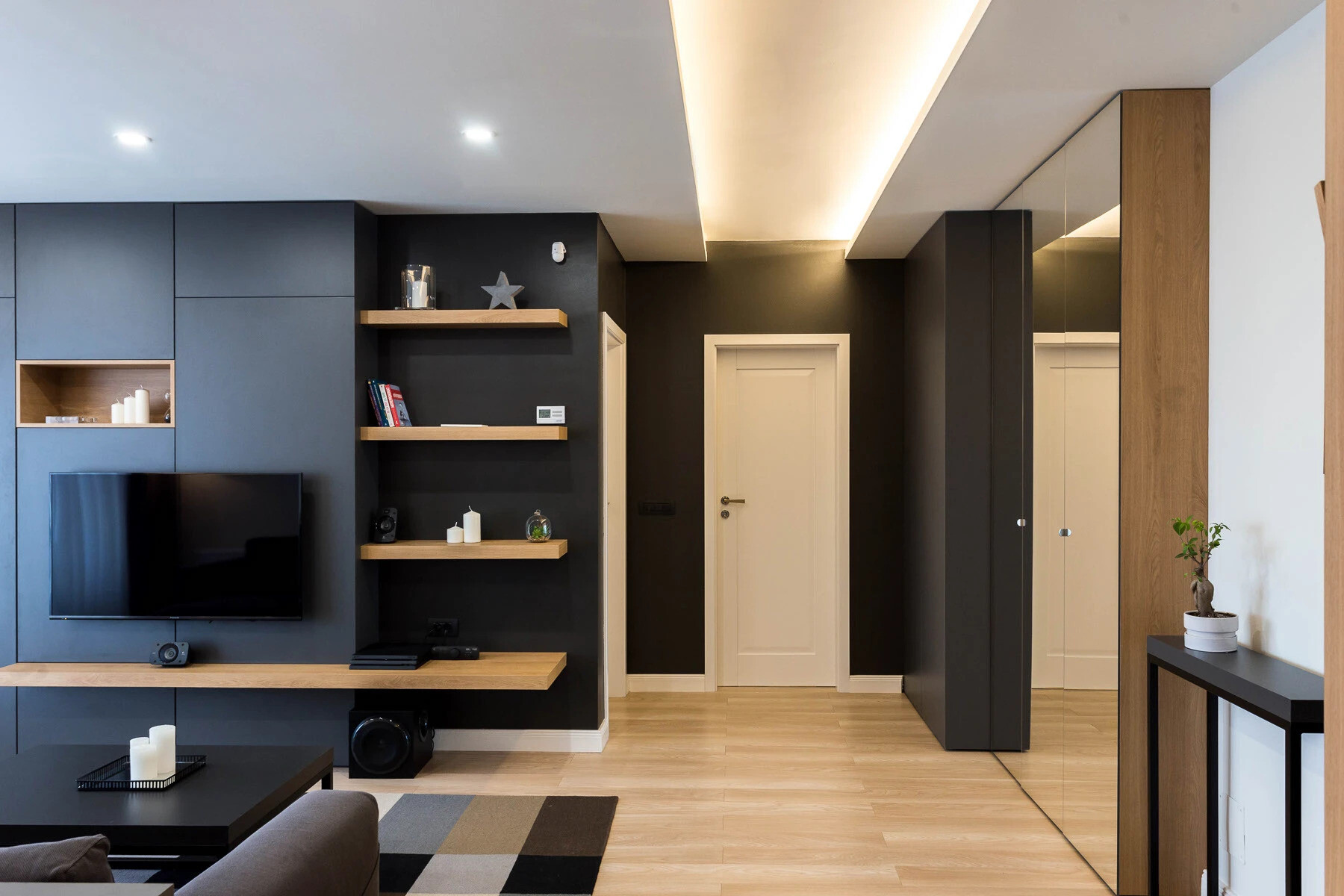 La sala de estar minimalista utiliza tonos cálidos de madera, paredes blancas y suaves tonos negros y grises para crear un espacio luminoso y tranquilo, perfecto para relajarse.