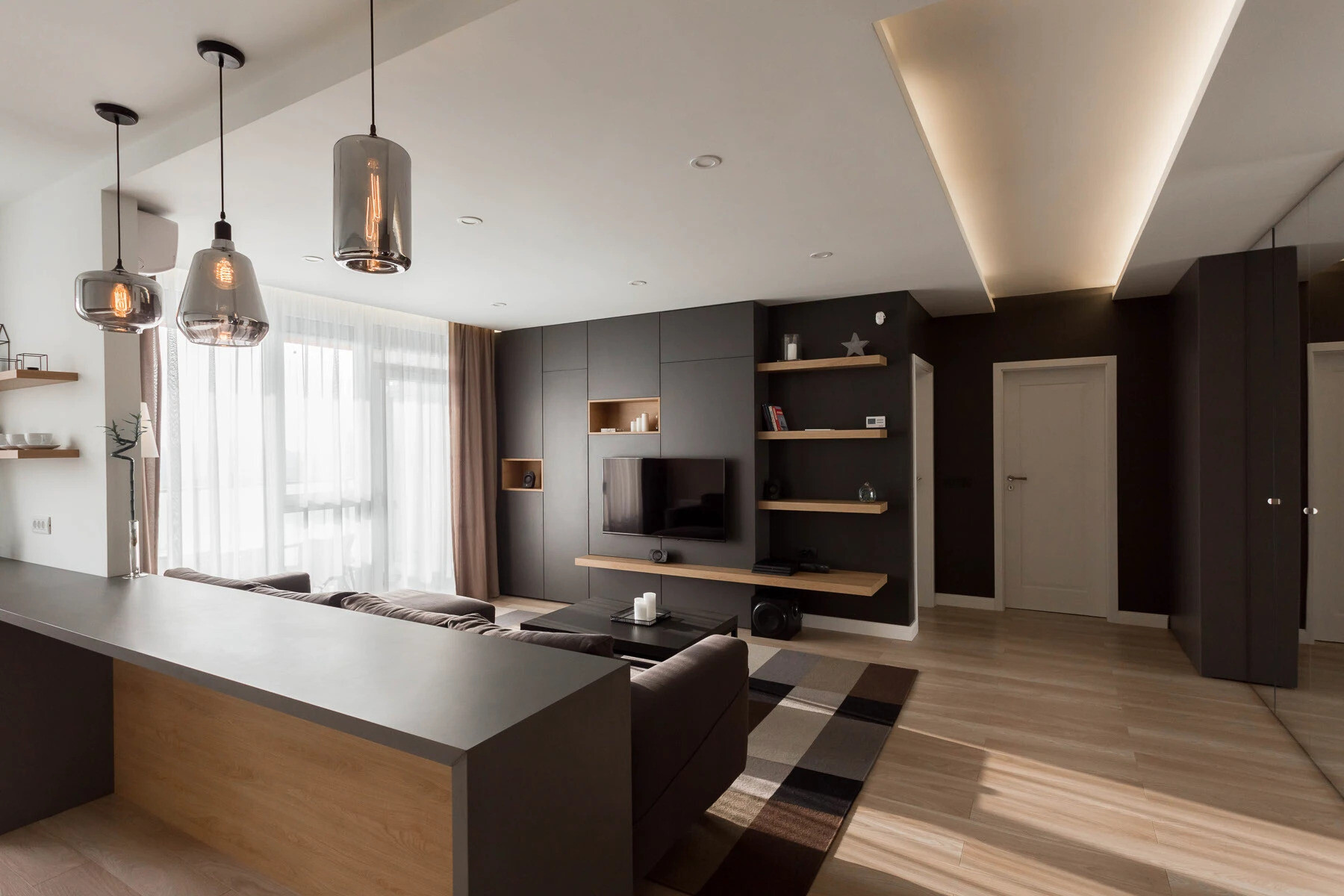 La sala de estar minimalista utiliza tonos cálidos de madera, paredes blancas y suaves tonos negros y grises para crear un espacio luminoso y tranquilo, perfecto para relajarse.