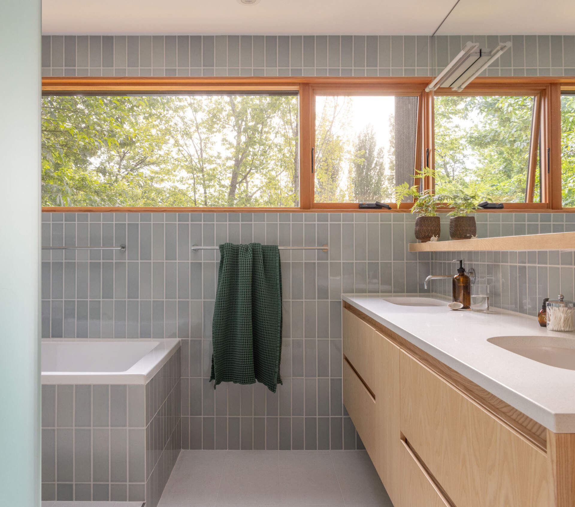 In the primary bath, Fireclay Hood River Gloss tile wraps the walls while Daltile Outlander Marine tile grounds the floor. Privacy glass, mirrors, and full height detailing emphasize height and brightness.