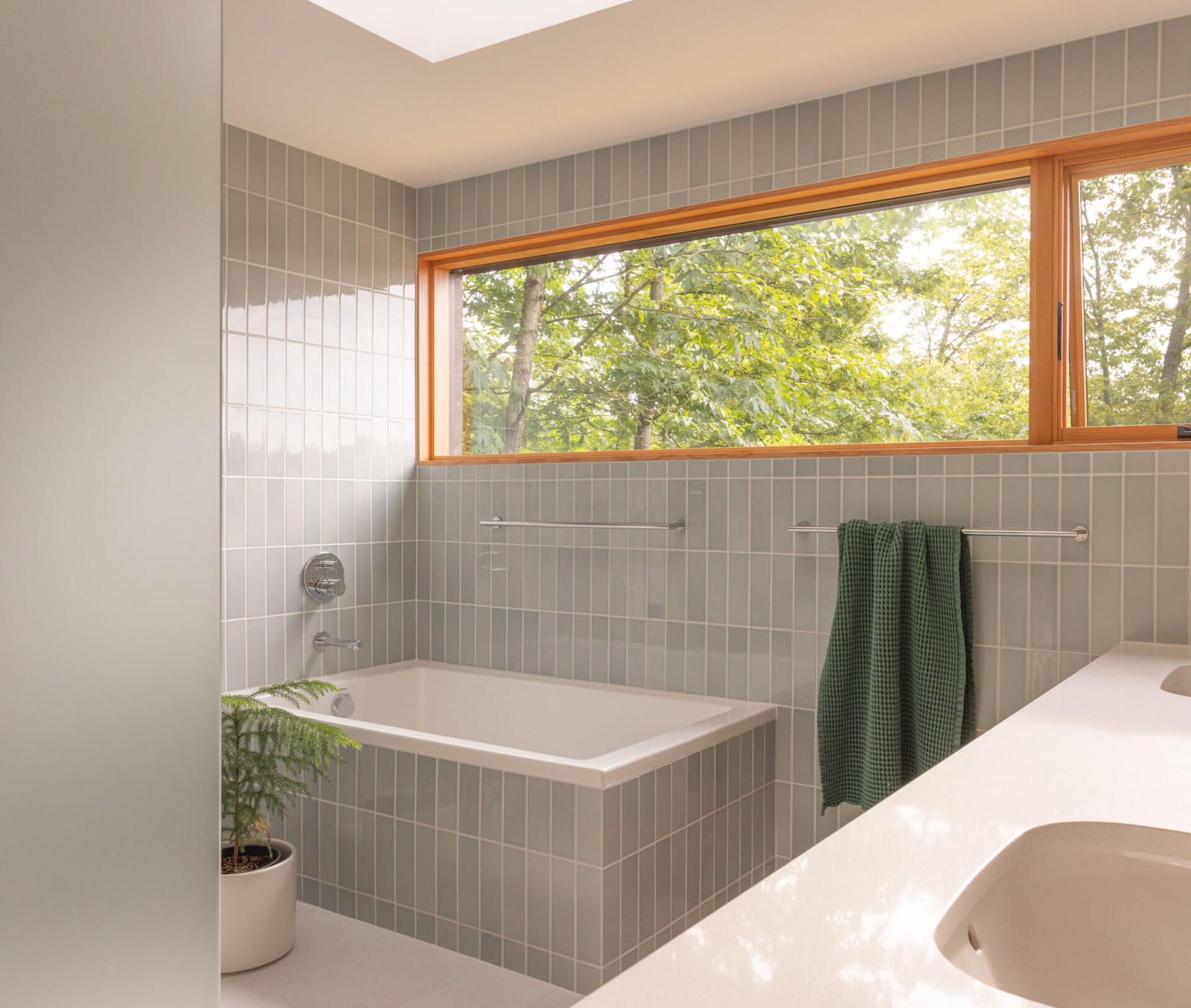 In the primary bath, Fireclay Hood River Gloss tile wraps the walls while Daltile Outlander Marine tile grounds the floor. Privacy glass, mirrors, and full height detailing emphasize height and brightness.