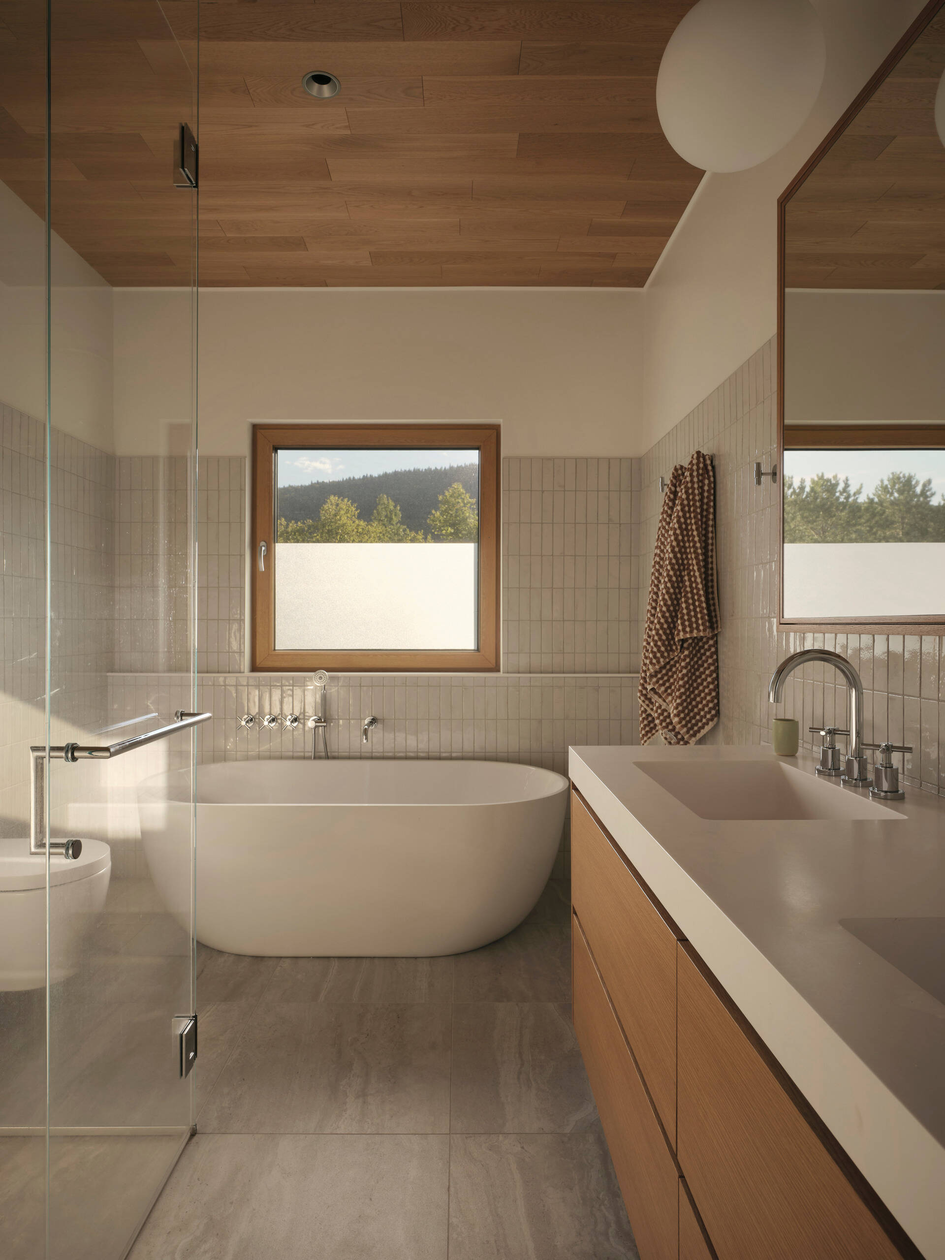 In this bathroom, vertical grey tiles have been combined with wood to create a balance of texture and tone, while the window allows sunlight to filter through, creating soft patterns across the surfaces. 