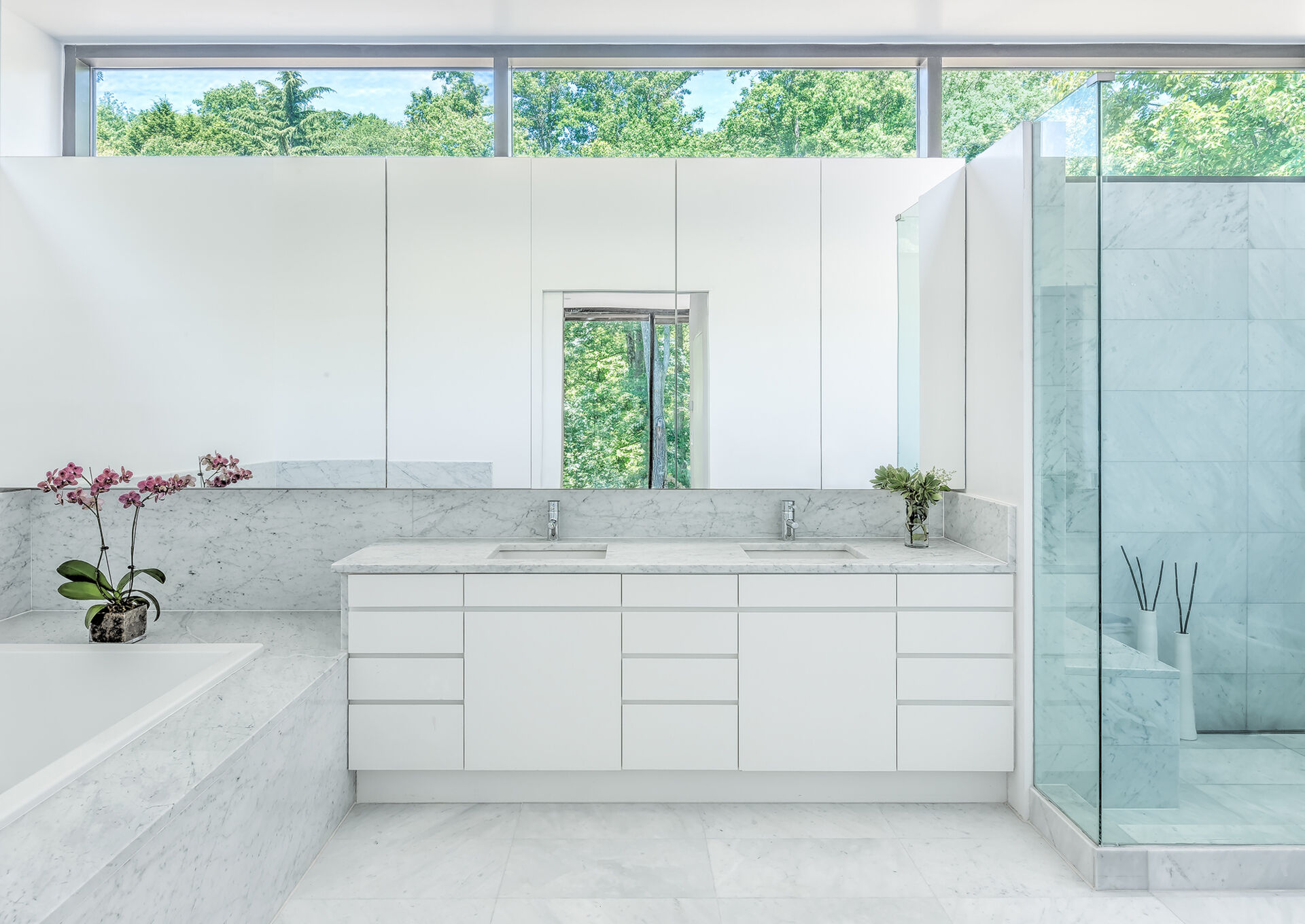 A bright, minimalist bathroom that reflects the light and serenity of its forest surroundings.