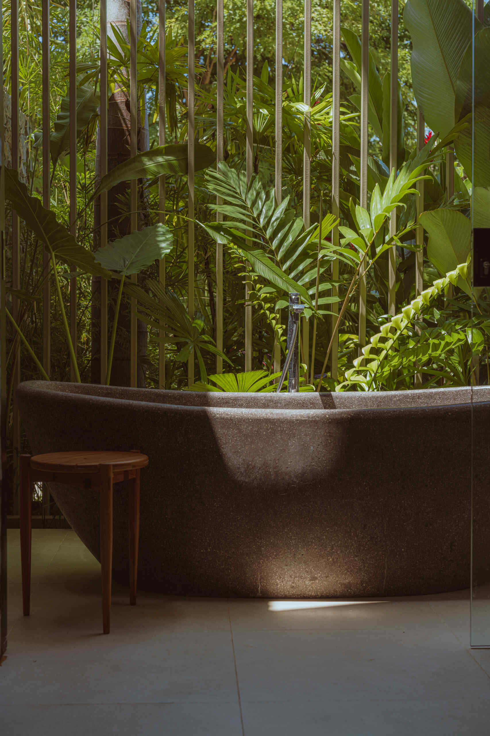 The bathroom features a long vanity topped with woven pendant lights that add warmth and texture. A freestanding bathtub sits nearby, surrounded by lush plants, creating a serene, spa-like corner that connects the space to the home’s natural surroundings.