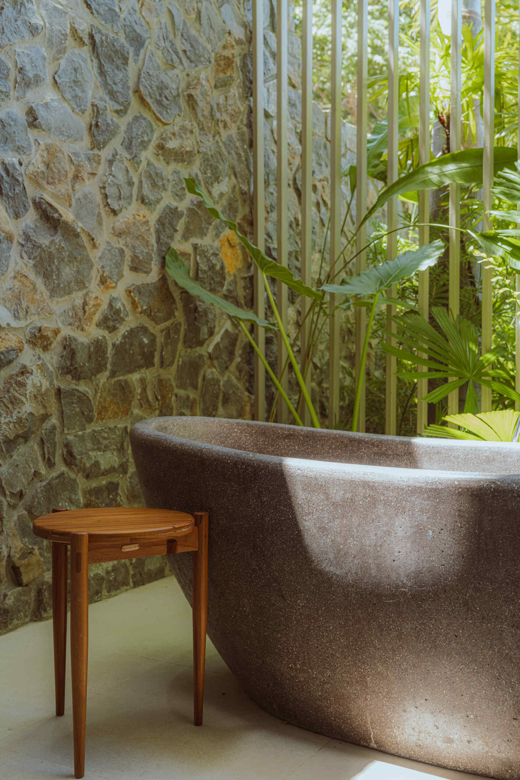 The bathroom features a long vanity topped with woven pendant lights that add warmth and texture. A freestanding bathtub sits nearby, surrounded by lush plants, creating a serene, spa-like corner that connects the space to the home’s natural surroundings.