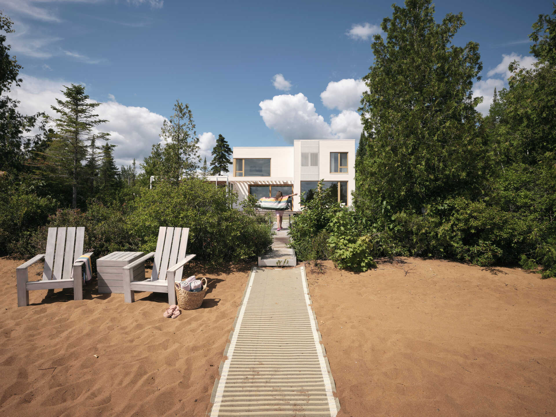 A stone path leads from the veranda through native plantings toward a fire pit and a sandy beach. 