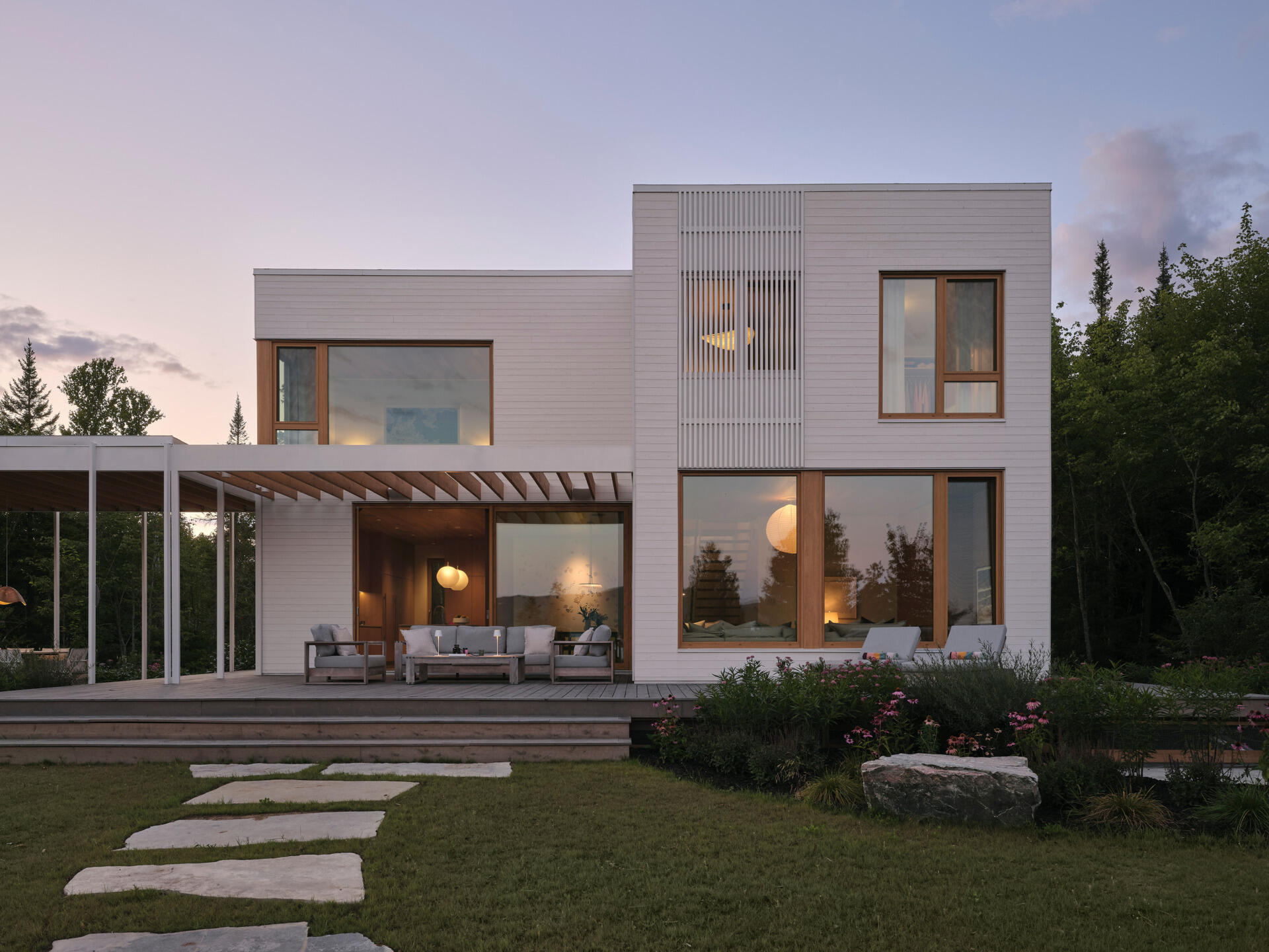 A stone path leads from the veranda through native plantings toward a fire pit and a sandy beach. 