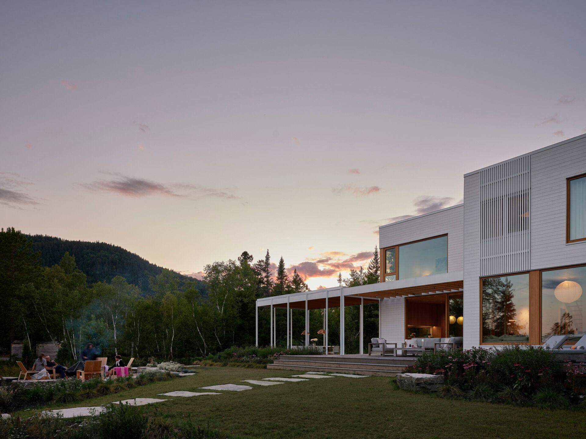 A stone path leads from the veranda through native plantings toward a fire pit and a sandy beach. 