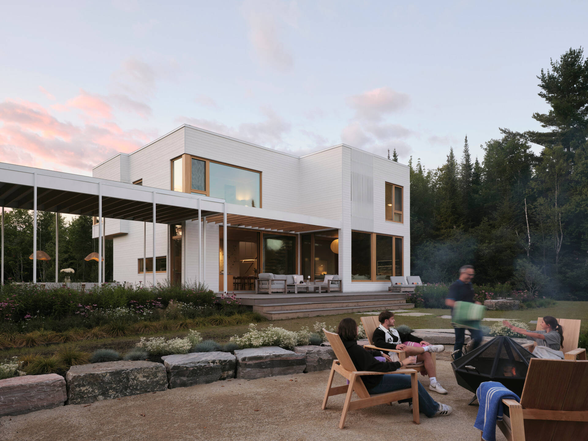 A stone path leads from the veranda through native plantings toward a fire pit and a sandy beach. 