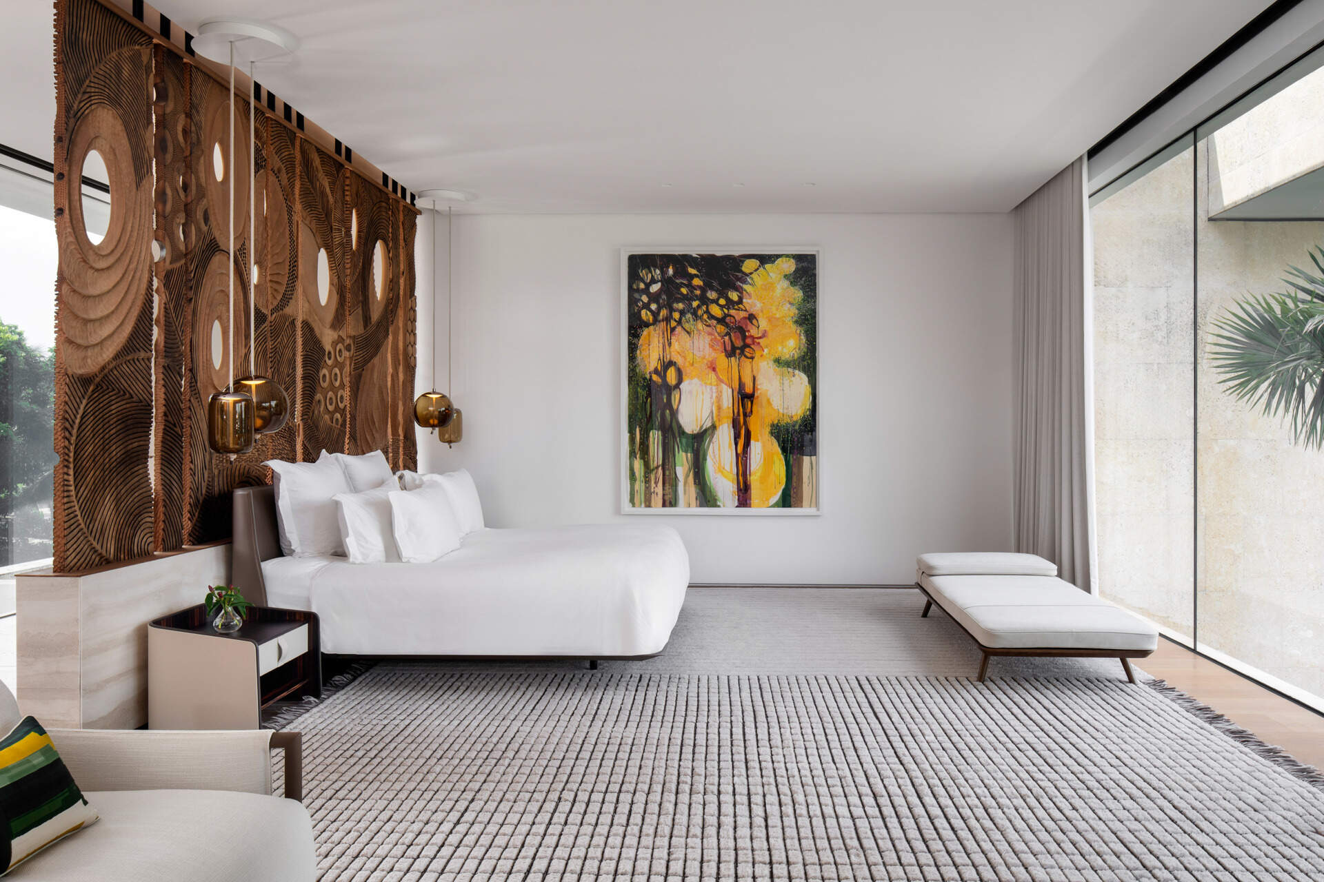 Interiors, like this bedroom, are filled with timber, stone, and local artwork create a warm contrast to the clean architecture.