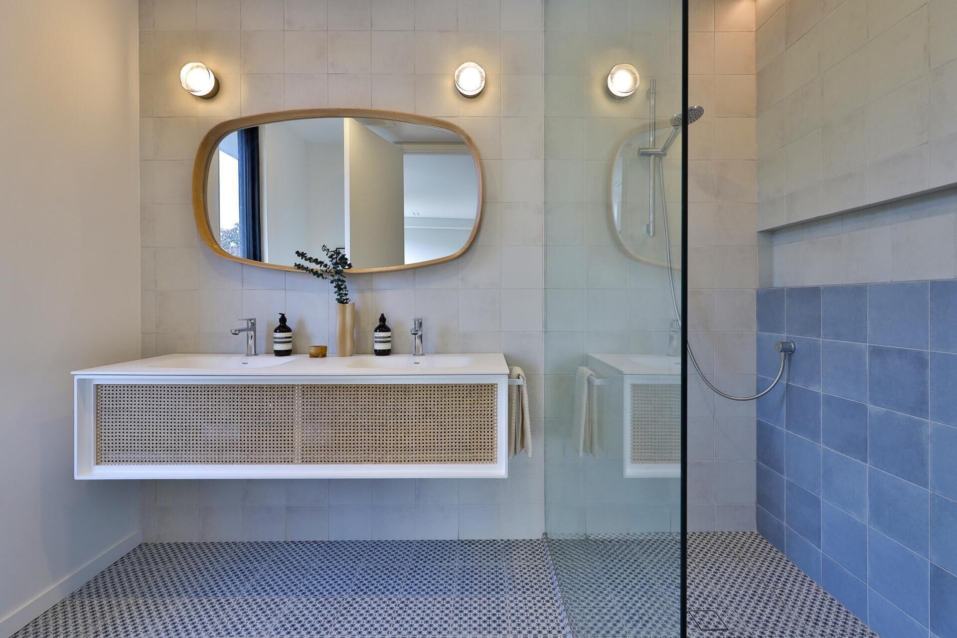Matte white and quarter cut oak built ins keep the palette calm. The bathroom unfolds in blue tones and subtle patterns that echo the home’s quiet material rigor.