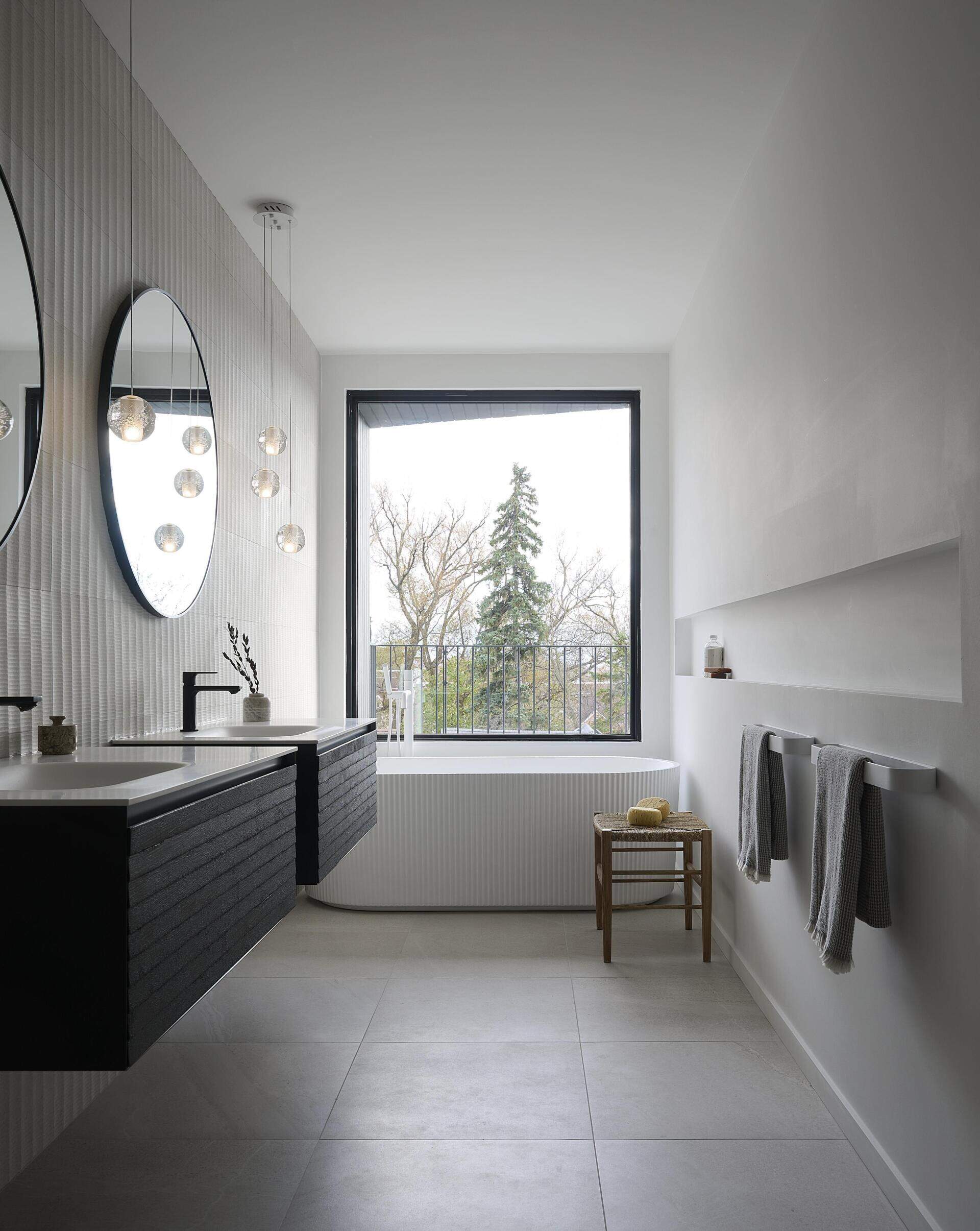 In this ensuite bathroom, a freestanding bathroom is positioned below the window, while large format tiles cover the floor, and a shelving niche lines the wall.