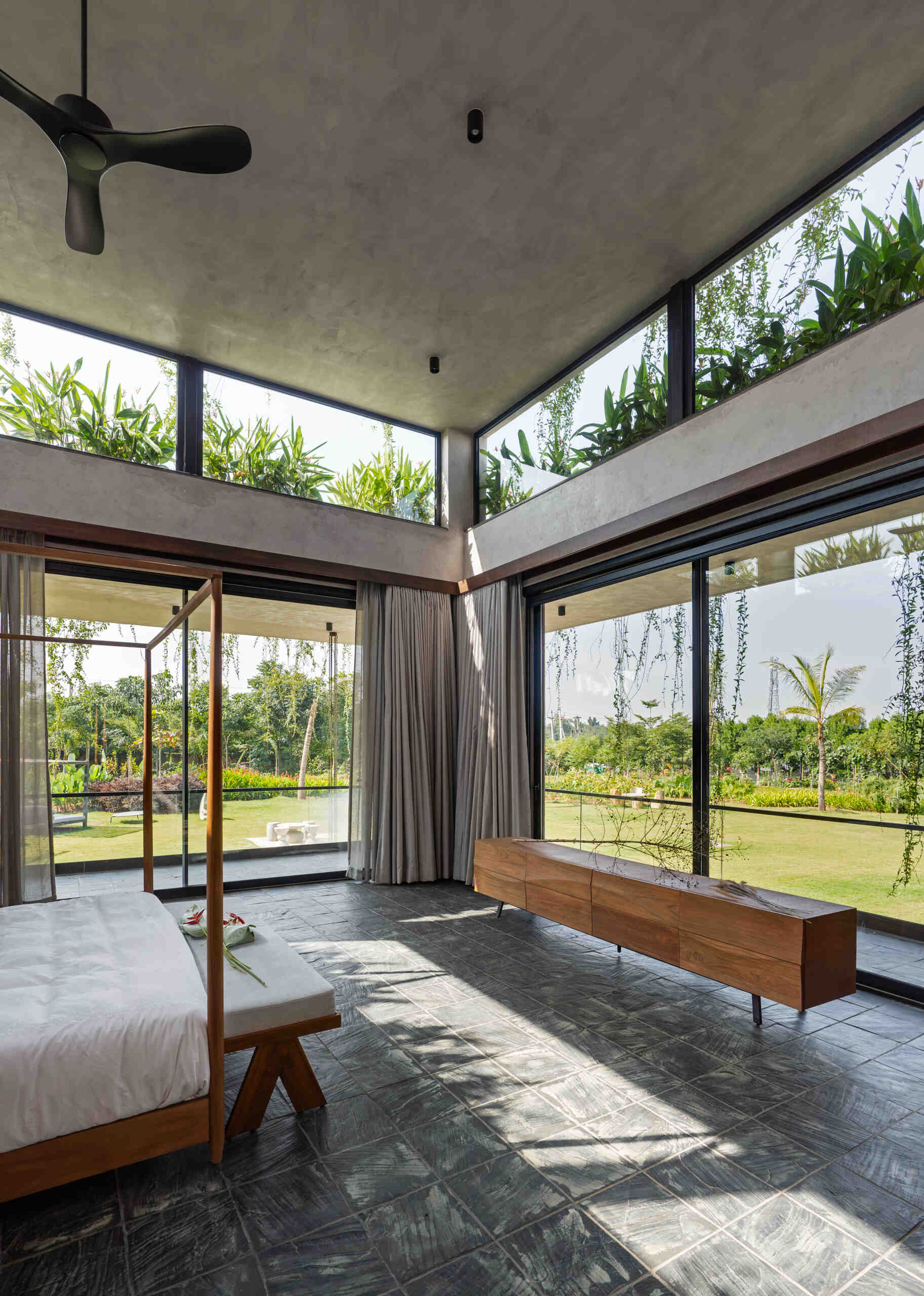 A modern bedroom framed by stone walls and large windows that welcome in light and greenery.