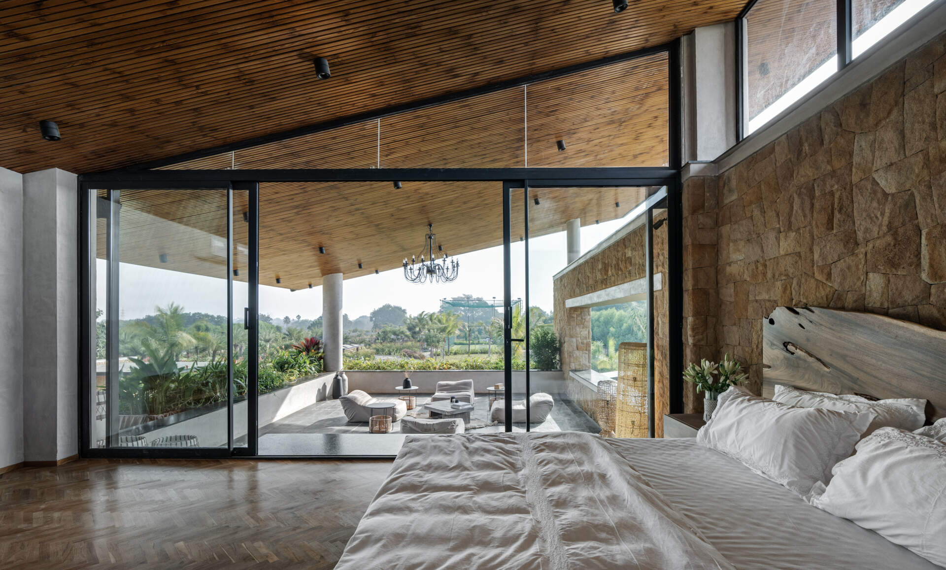 A modern bedroom framed by stone walls and large windows that welcome in light and greenery.
