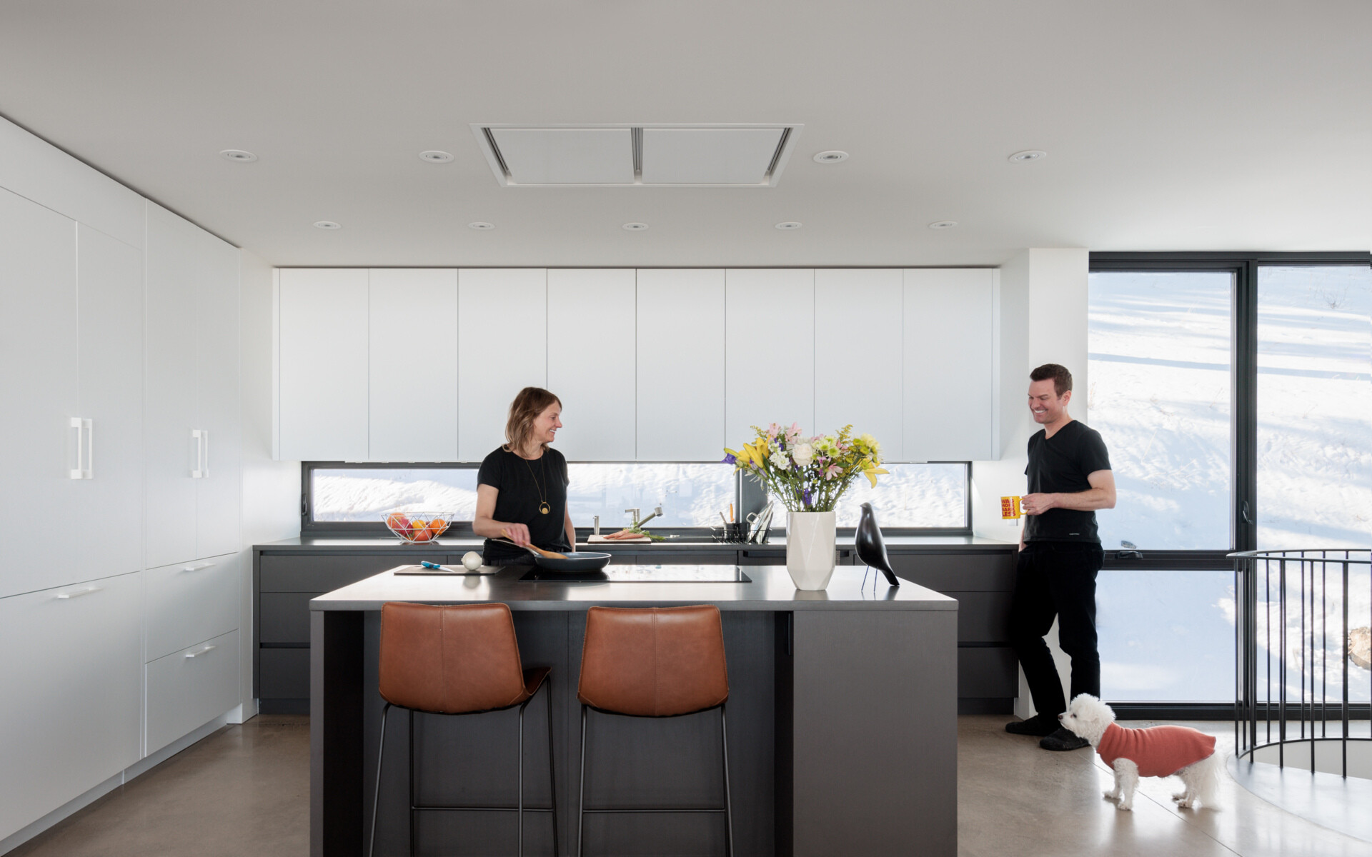Daylight fills the kitchen, reducing reliance on artificial lighting and keeping the upper floor airy and open, while the black and white cabinets create contrast, and horizontal windows act as a backsplash. 
