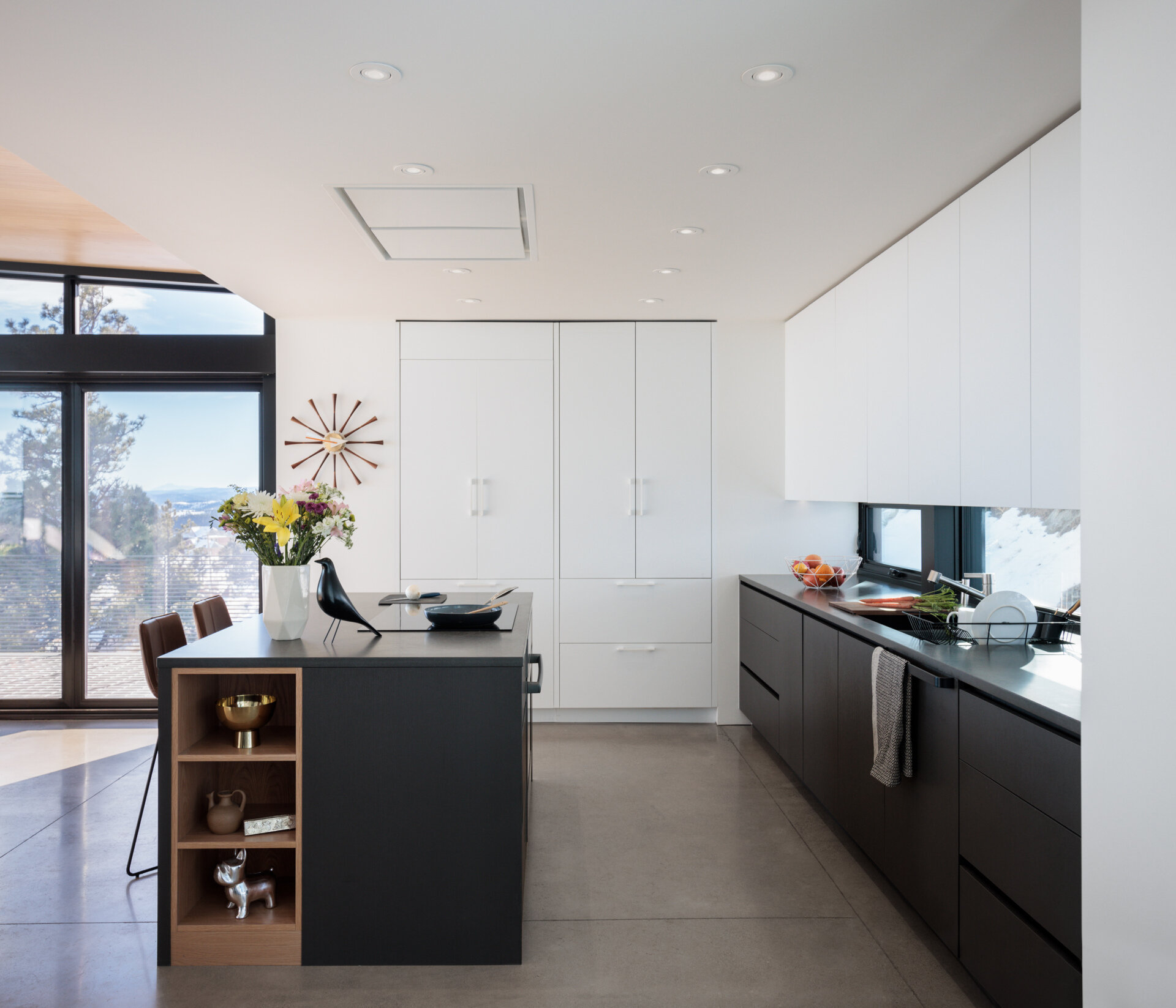 Daylight fills the kitchen, reducing reliance on artificial lighting and keeping the upper floor airy and open, while the black and white cabinets create contrast, and horizontal windows act as a backsplash. 