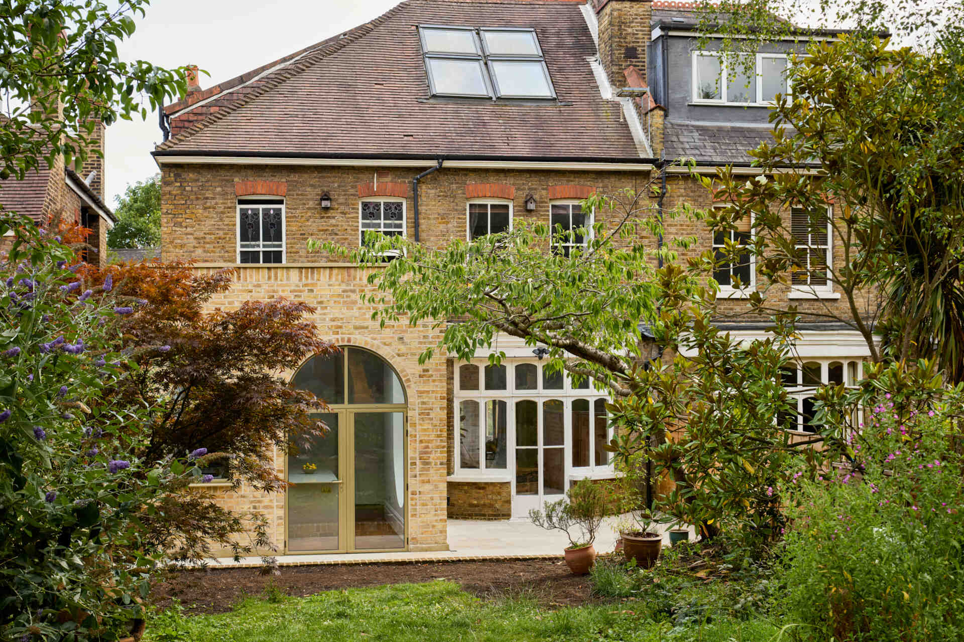 This rear extension of Perry Vale House reinterprets Edwardian craftsmanship with playful arches, reclaimed yellow London Stock Brick, and metallic bronze framing.