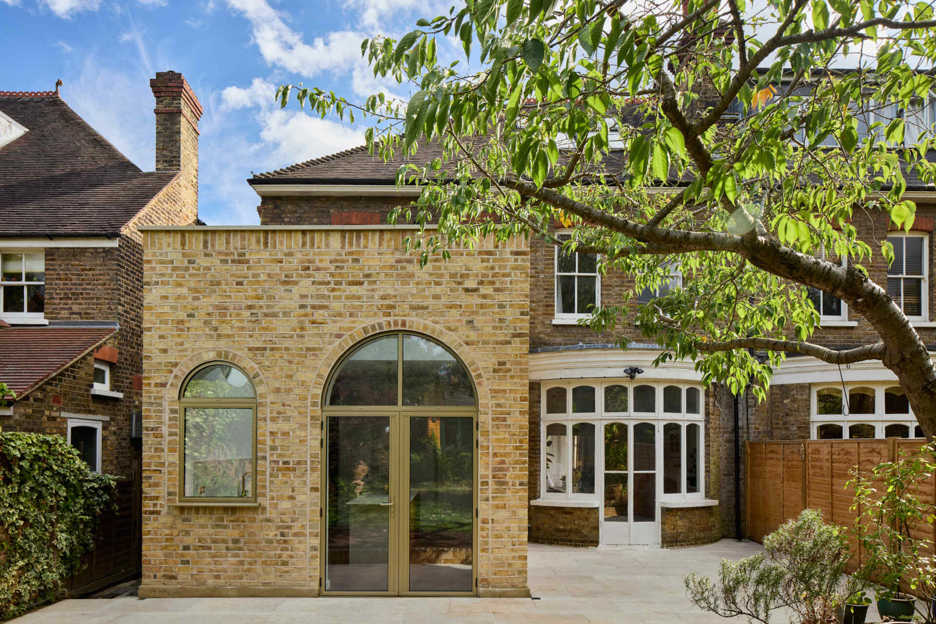 This rear extension of Perry Vale House reinterprets Edwardian craftsmanship with playful arches, reclaimed yellow London Stock Brick, and metallic bronze framing.