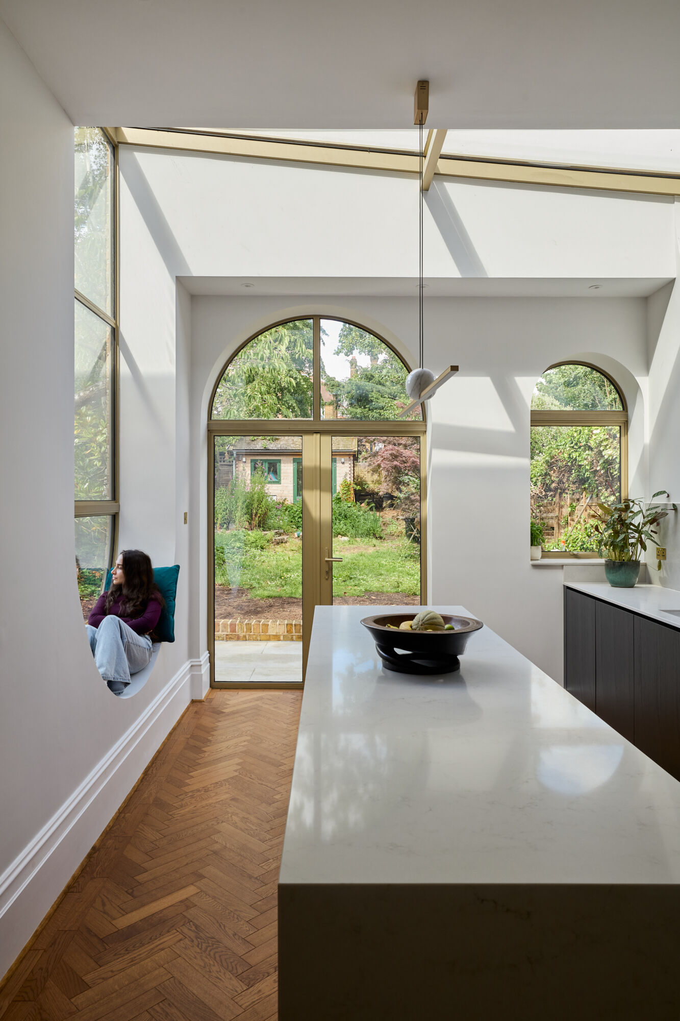 In the kitchen of Perry Vale House, inverted arches and a wraparound glass roof fill the space with natural light. Soft grey cabinetry, marble worktops, and timber tones create a warm, modern feel that stays true to the home’s character.