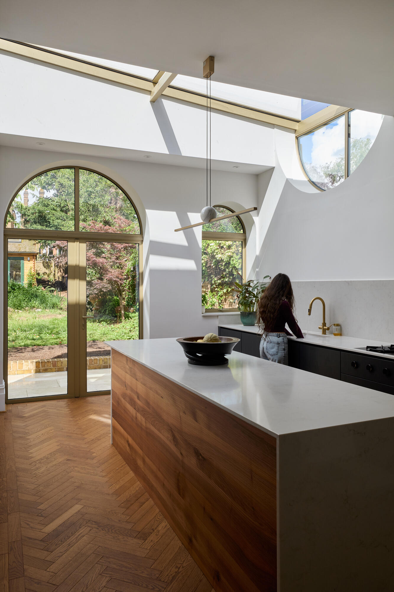 In the kitchen of Perry Vale House, inverted arches and a wraparound glass roof fill the space with natural light. Soft grey cabinetry, marble worktops, and timber tones create a warm, modern feel that stays true to the home’s character.