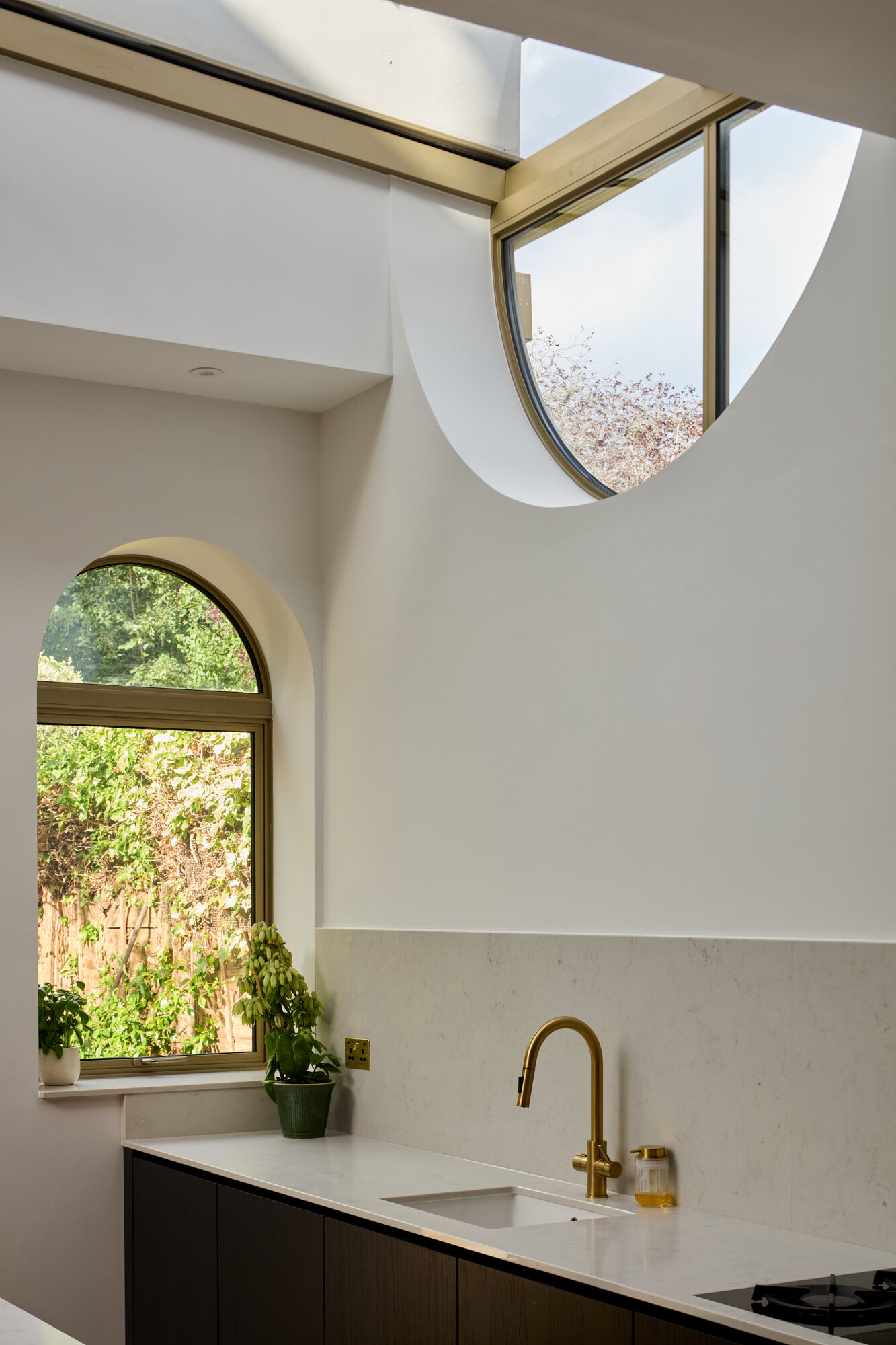 In the kitchen of Perry Vale House, inverted arches and a wraparound glass roof fill the space with natural light. Soft grey cabinetry, marble worktops, and timber tones create a warm, modern feel that stays true to the home’s character.