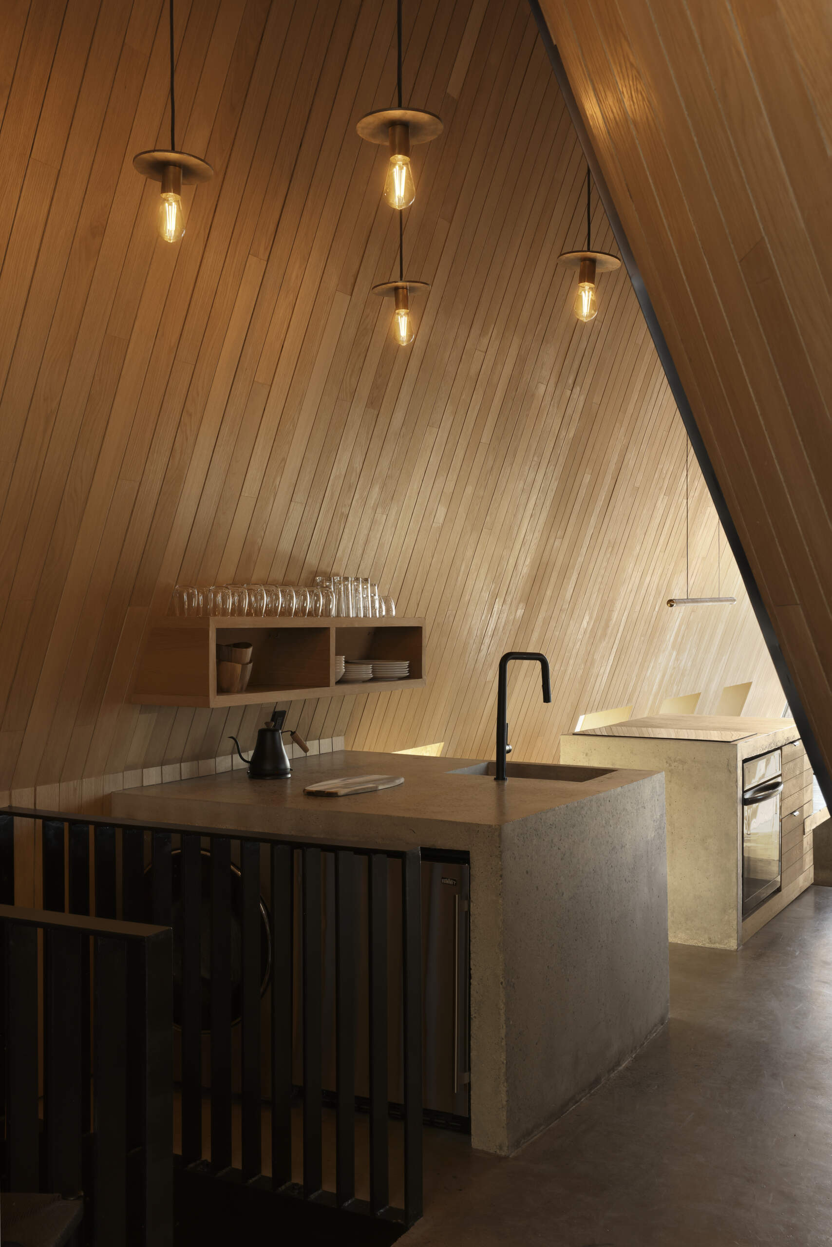 Inside this modern cottage, the atmosphere is warm and simple with white oak clad walls and polished concrete floors. The great room is organized into three zones for gathering, eating, and cooking, each set at its own elevation.