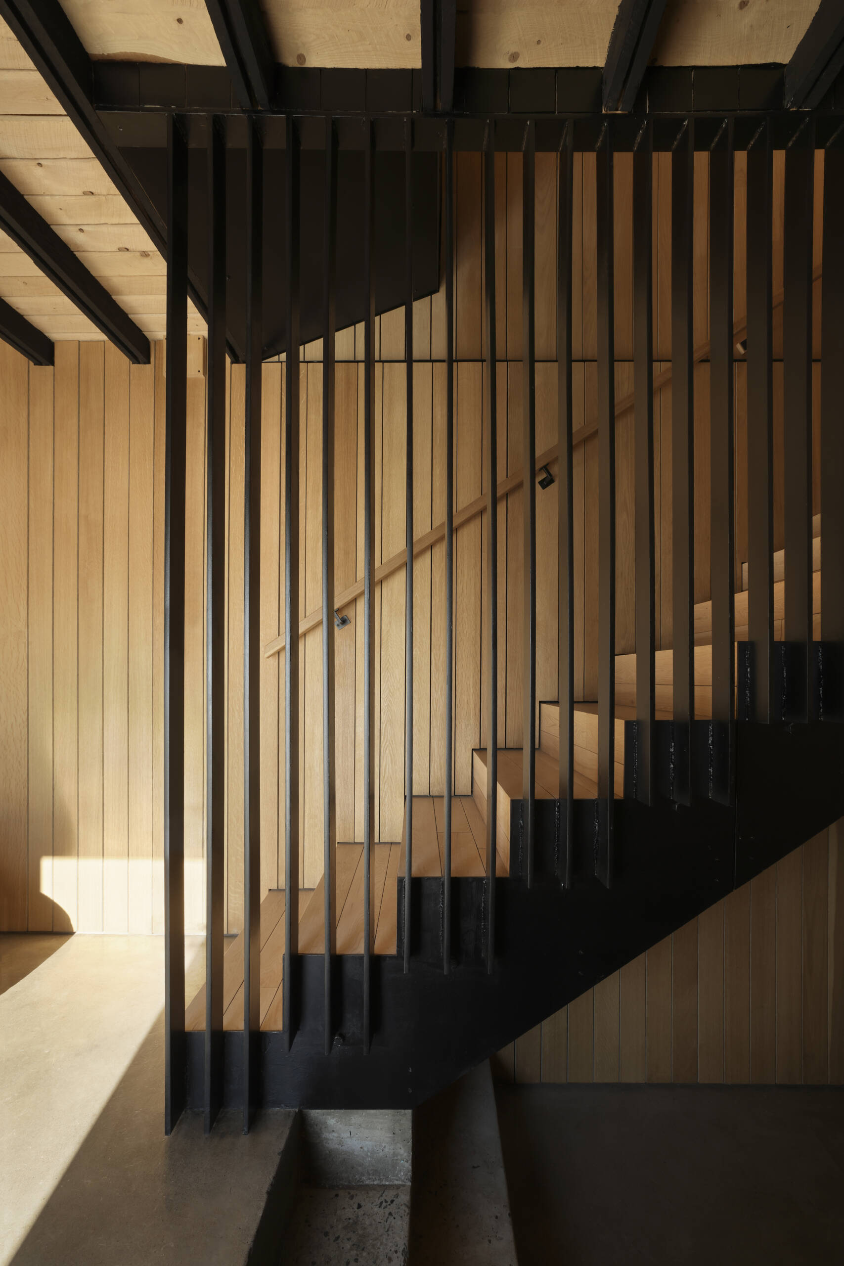 Inside this modern cottage, the atmosphere is warm and simple with white oak clad walls and polished concrete floors. The great room is organized into three zones for gathering, eating, and cooking, each set at its own elevation.