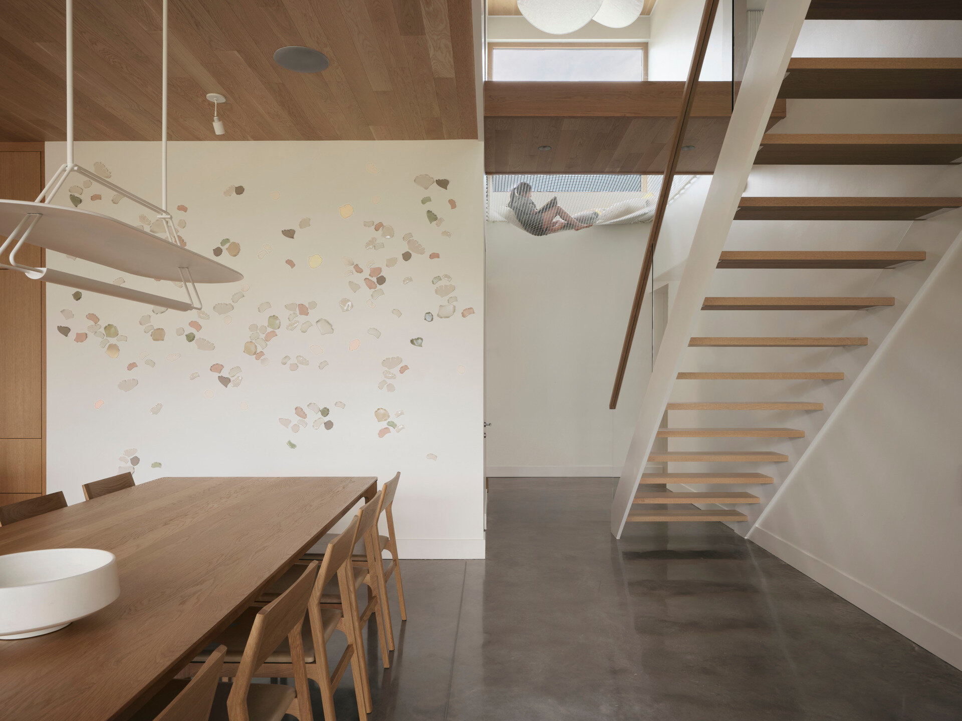 A light-filled staircase connects the different levels, with pale wood steps echoing the natural palette used throughout the home. Above, a suspended net loft creates a cozy nook for reading or daydreaming.