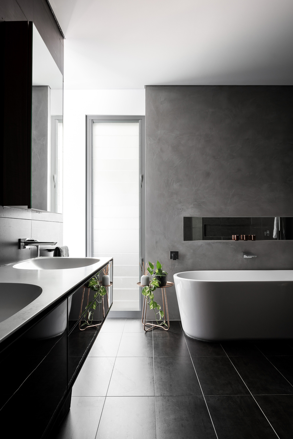 A smartly detailed bathroom with a black vanity, matching tiles, a white freestanding bath and a gentle grey accent wall.