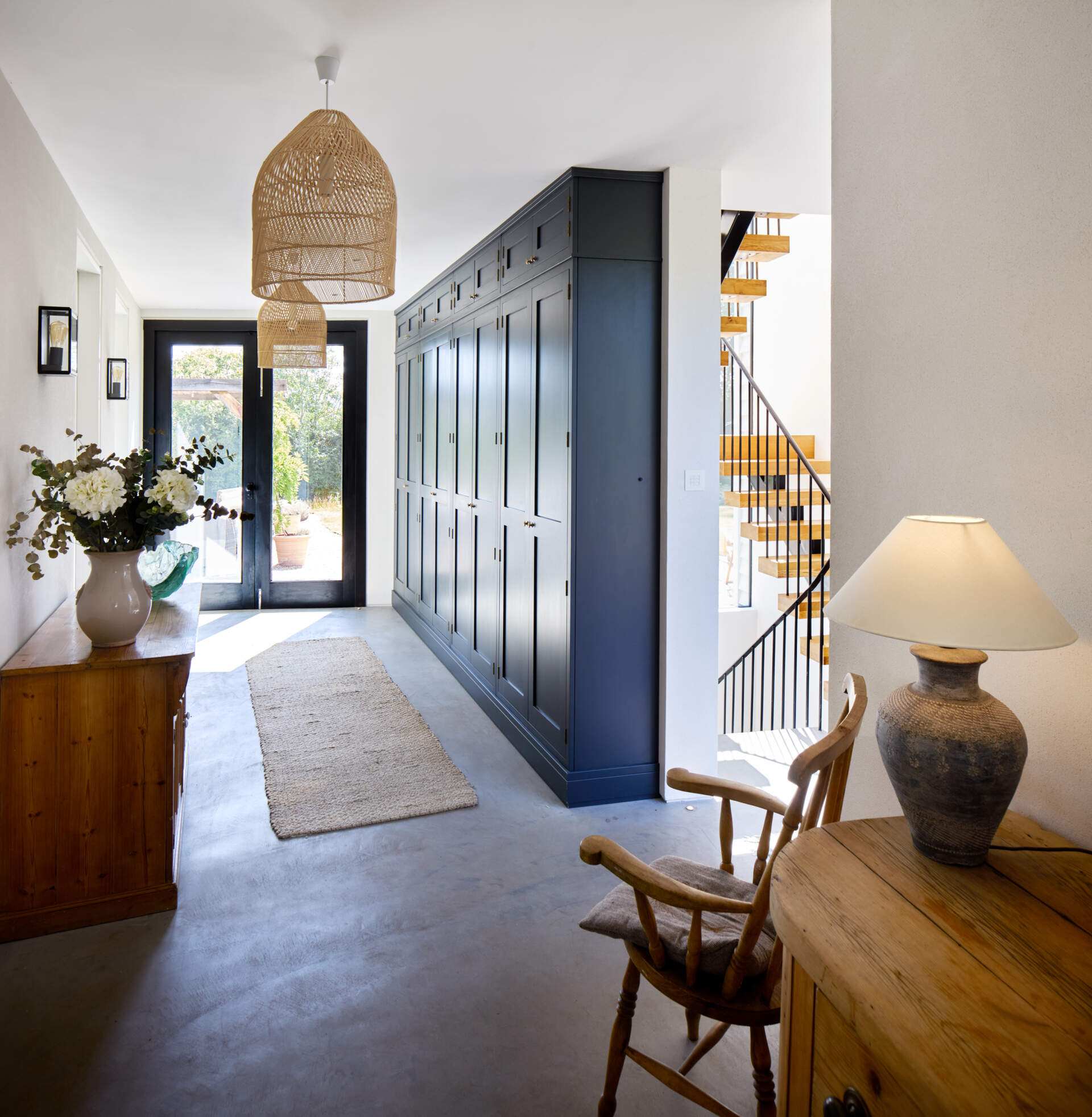 Inside this contemporary entryway, a wall of custom cabinetry lines the wall, while overhead, woven lamps add a textural element.