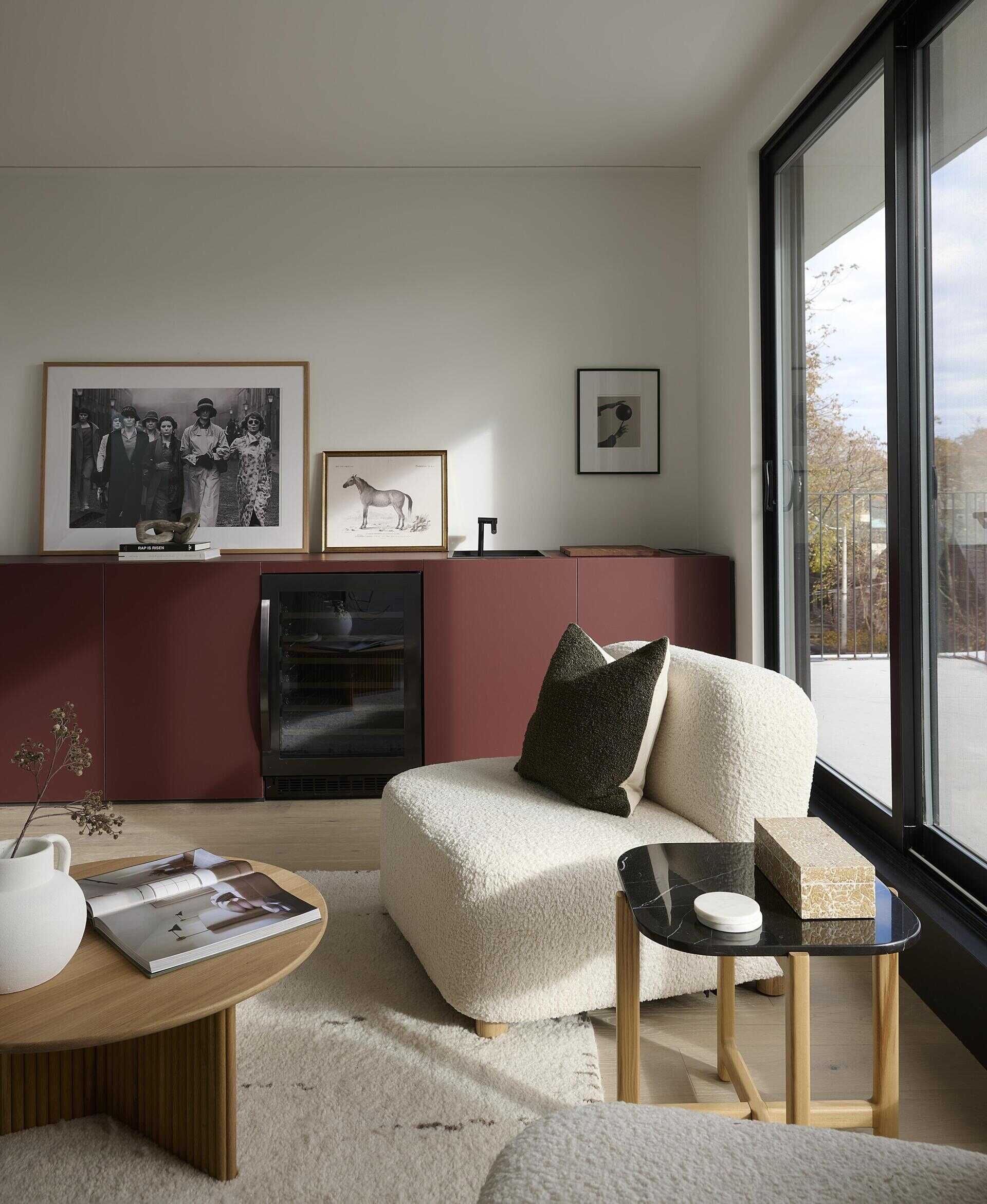 At the top of the home, a family room connects to the rooftop deck through a full glass wall, while a deep burgundy bar anchors the space, giving weight to the open view and complementing the calm interior palette.