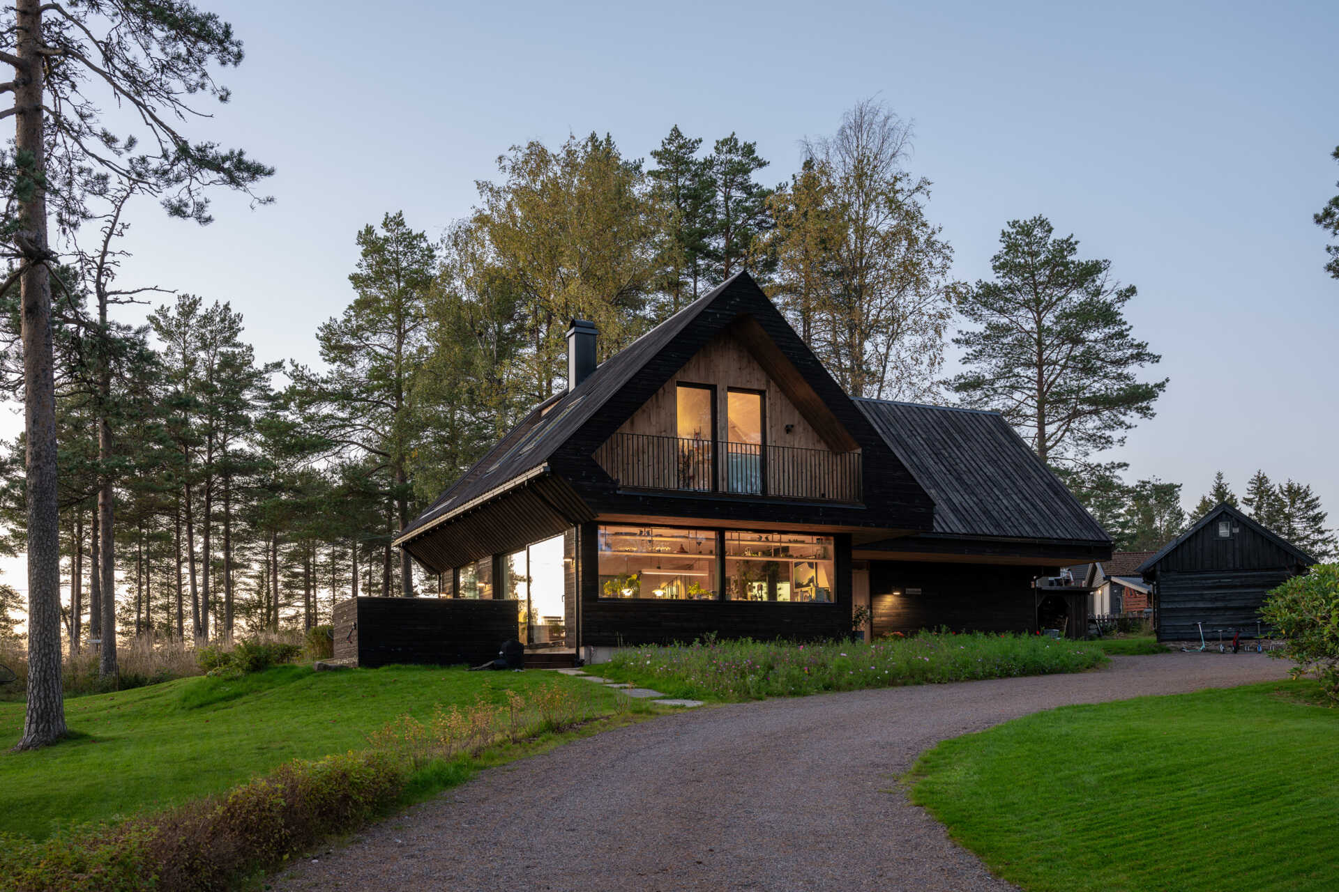 The house features a cross-gabled roof, dark timber cladding, and extended eaves, designed to harmonize with the surrounding pine forest.