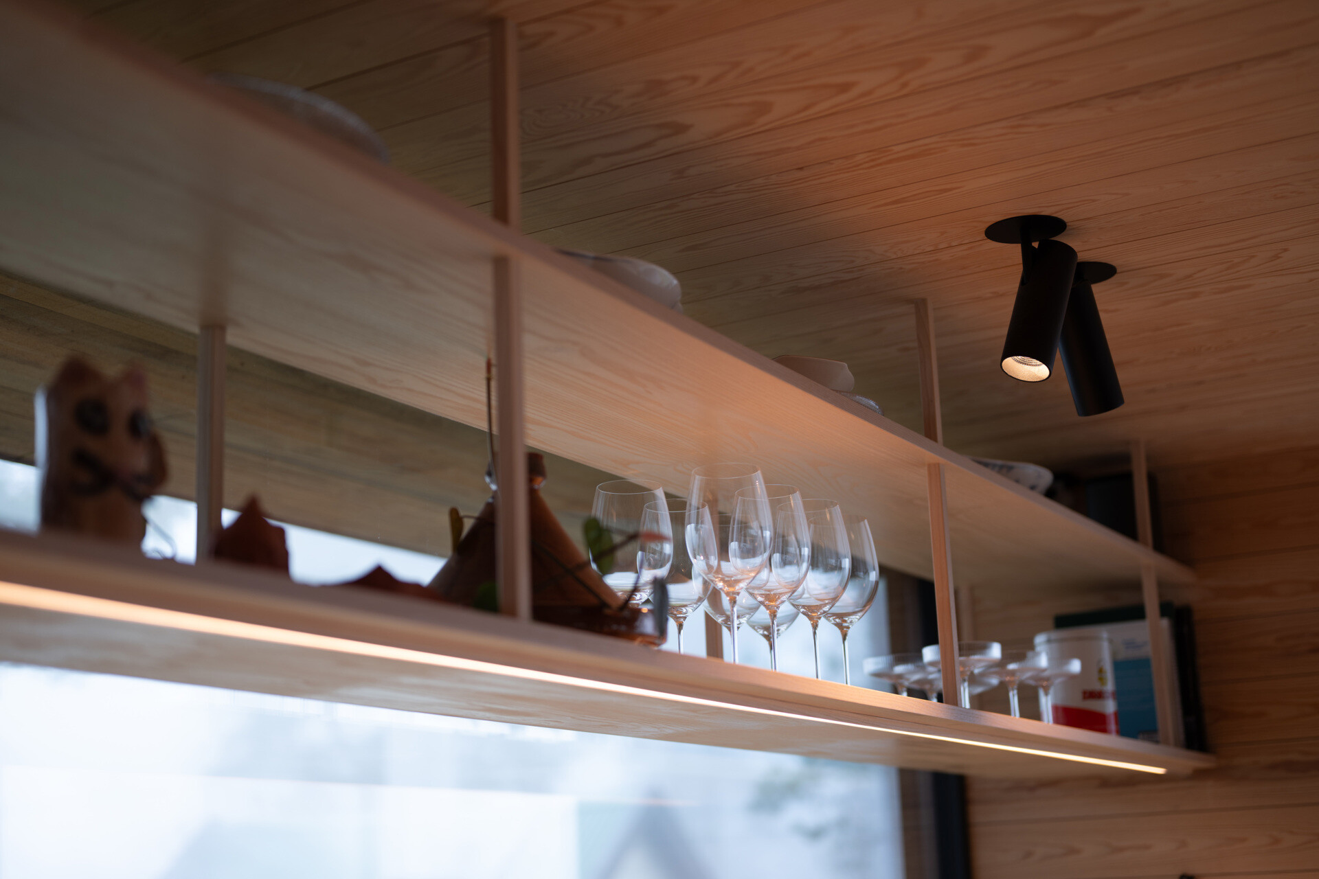 The kitchen, with hanging open shelving, is designed for efficiency and adaptability. Built-in storage and practical work surfaces ensure that daily routines are simple, while the timber finishes maintain warmth and texture.