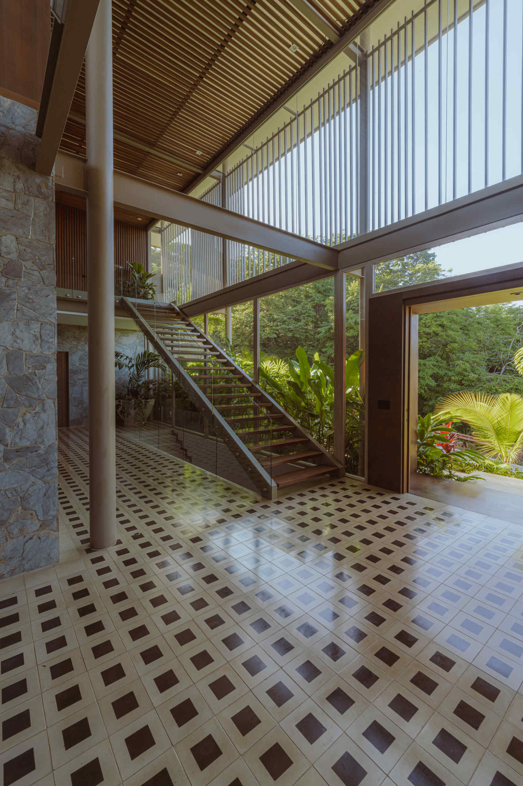 Inside the foyer, black and white tiles reference traditional Costa Rican patterns and connect the home to local craft. Cobalt blue armchairs introduce a bold moment of color that mirrors the tones of the sky and connects the interior to the surrounding landscape. From here, stairs guide the journey upward. The ascent reflects the concept of the home, with each step revealing wider views and lighter materials.
