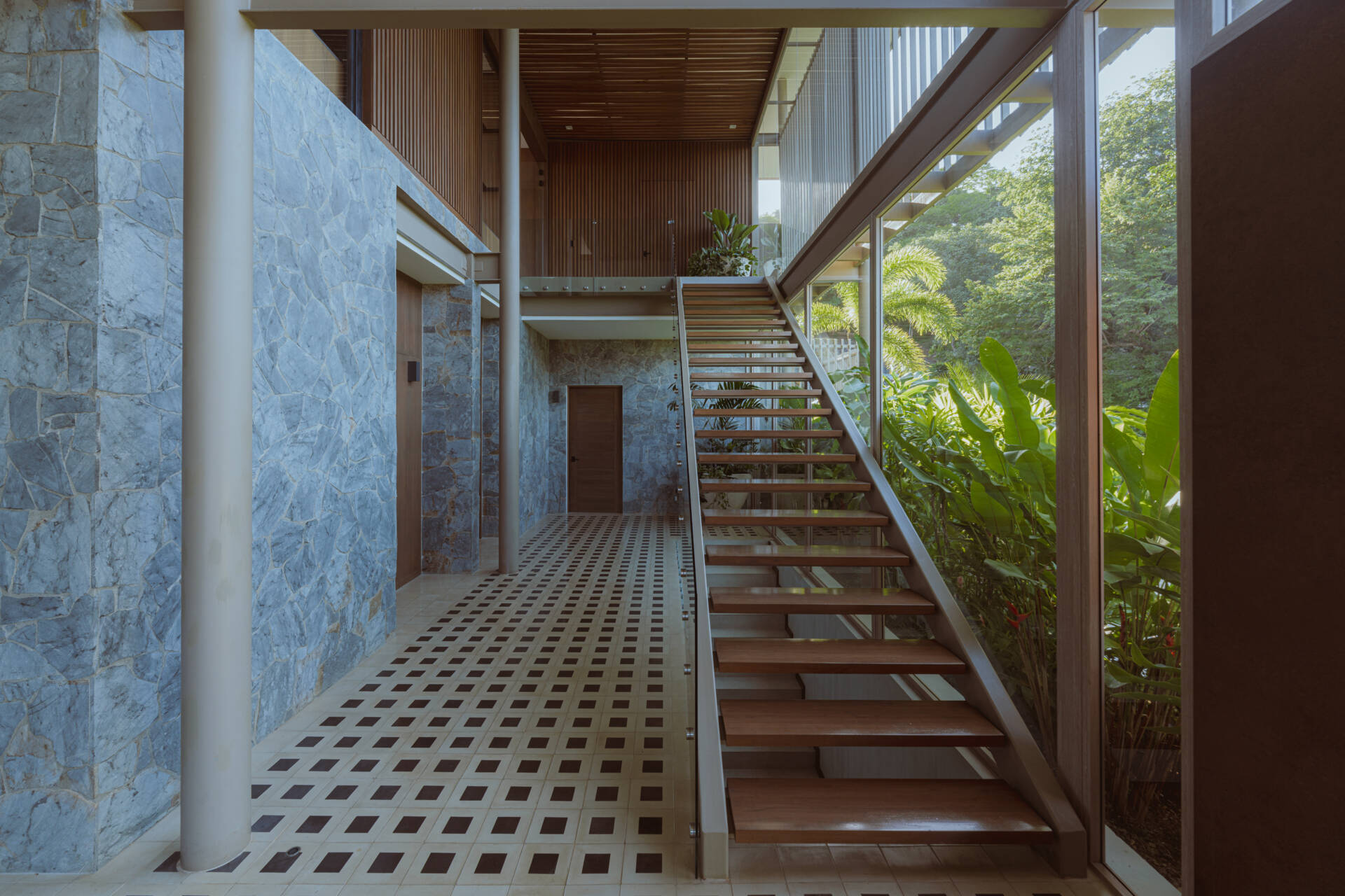 Inside the foyer, black and white tiles reference traditional Costa Rican patterns and connect the home to local craft. Cobalt blue armchairs introduce a bold moment of color that mirrors the tones of the sky and connects the interior to the surrounding landscape. From here, stairs guide the journey upward. The ascent reflects the concept of the home, with each step revealing wider views and lighter materials.