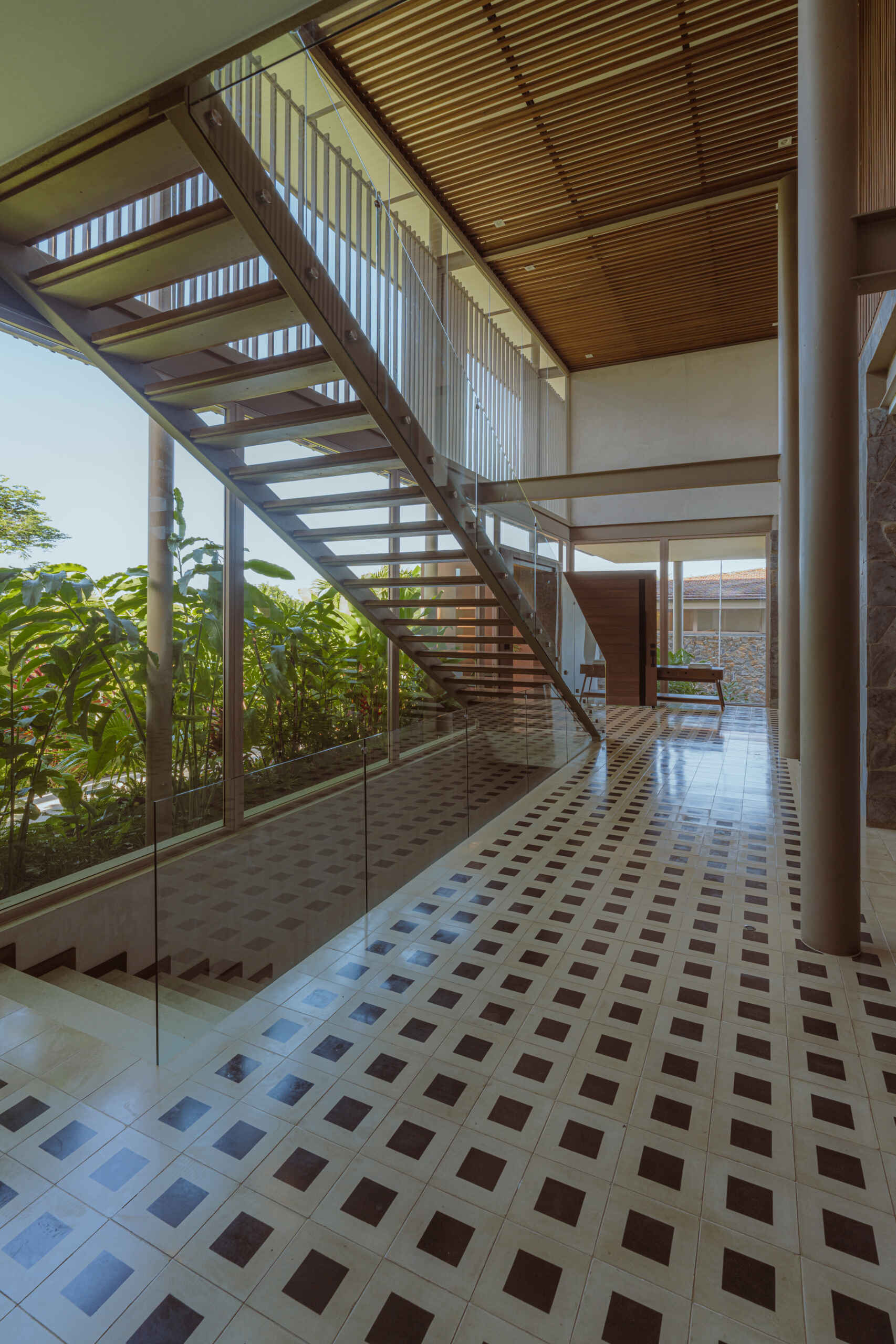 Inside the foyer, black and white tiles reference traditional Costa Rican patterns and connect the home to local craft. Cobalt blue armchairs introduce a bold moment of color that mirrors the tones of the sky and connects the interior to the surrounding landscape. From here, stairs guide the journey upward. The ascent reflects the concept of the home, with each step revealing wider views and lighter materials.