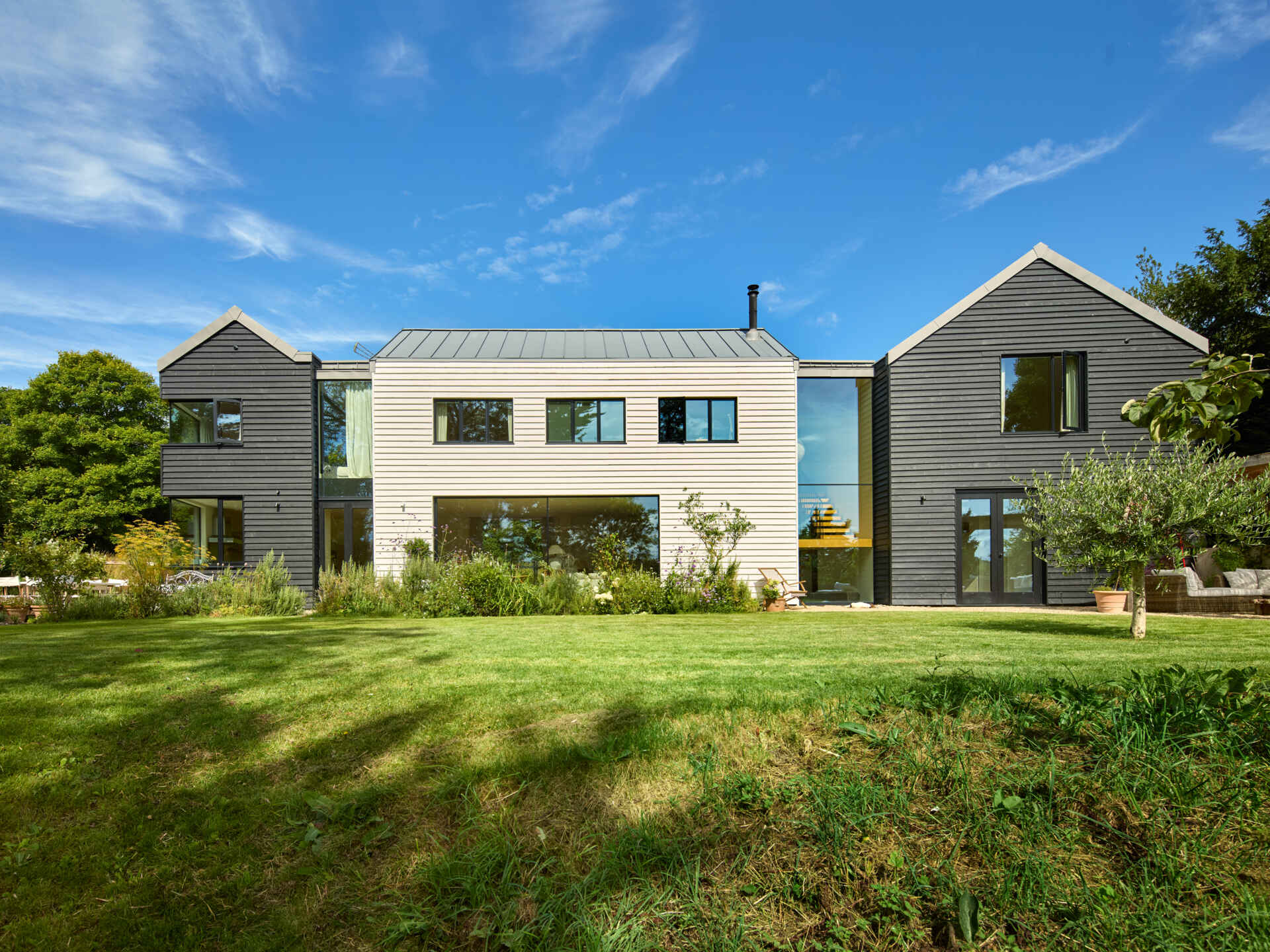 This rural home features dark timber that wraps the outer volumes, while a white central volume introduces a clear contrast. Zinc standing seam roofs complete the contemporary interpretation of traditional rural forms.