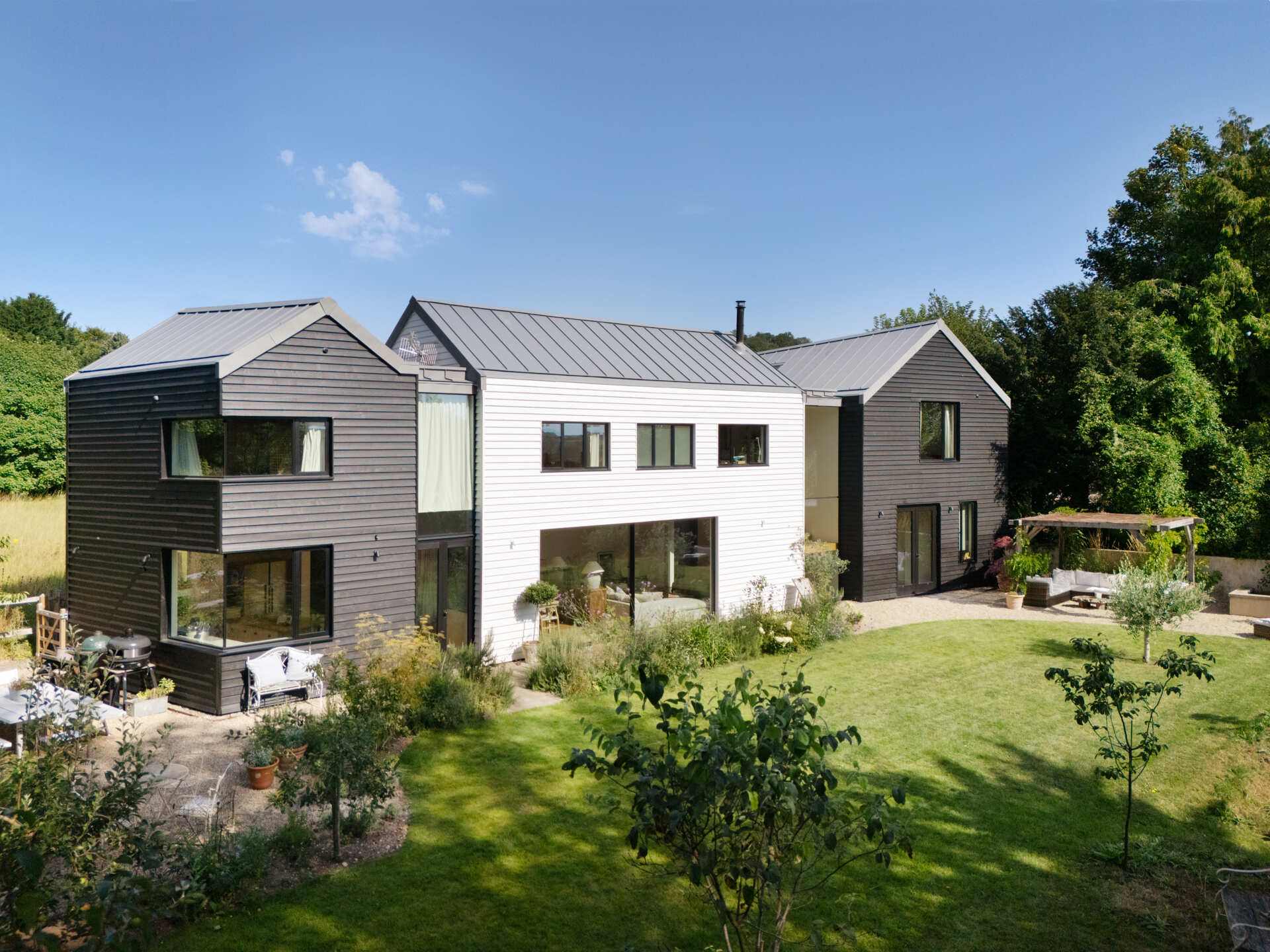 This rural home features dark timber that wraps the outer volumes, while a white central volume introduces a clear contrast. Zinc standing seam roofs complete the contemporary interpretation of traditional rural forms.