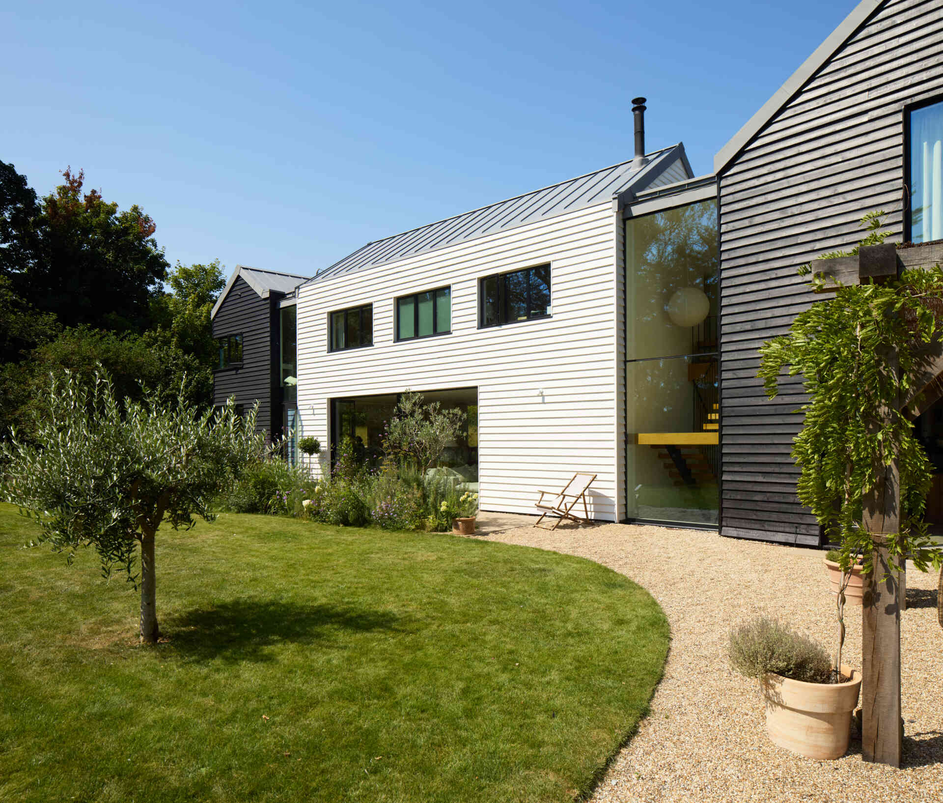 This rural home features dark timber that wraps the outer volumes, while a white central volume introduces a clear contrast. Zinc standing seam roofs complete the contemporary interpretation of traditional rural forms.