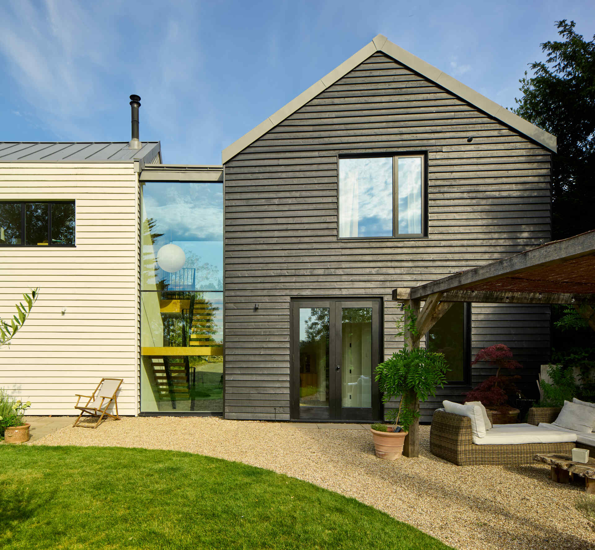 This rural home features dark timber that wraps the outer volumes, while a white central volume introduces a clear contrast. Zinc standing seam roofs complete the contemporary interpretation of traditional rural forms.