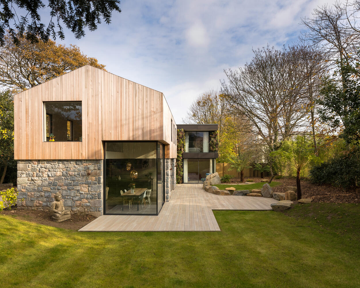 This modern home is wrapped in Guernsey granite, cedar cladding, and a living wall with 13 native species that soften the structure and blend it into the forested setting.
