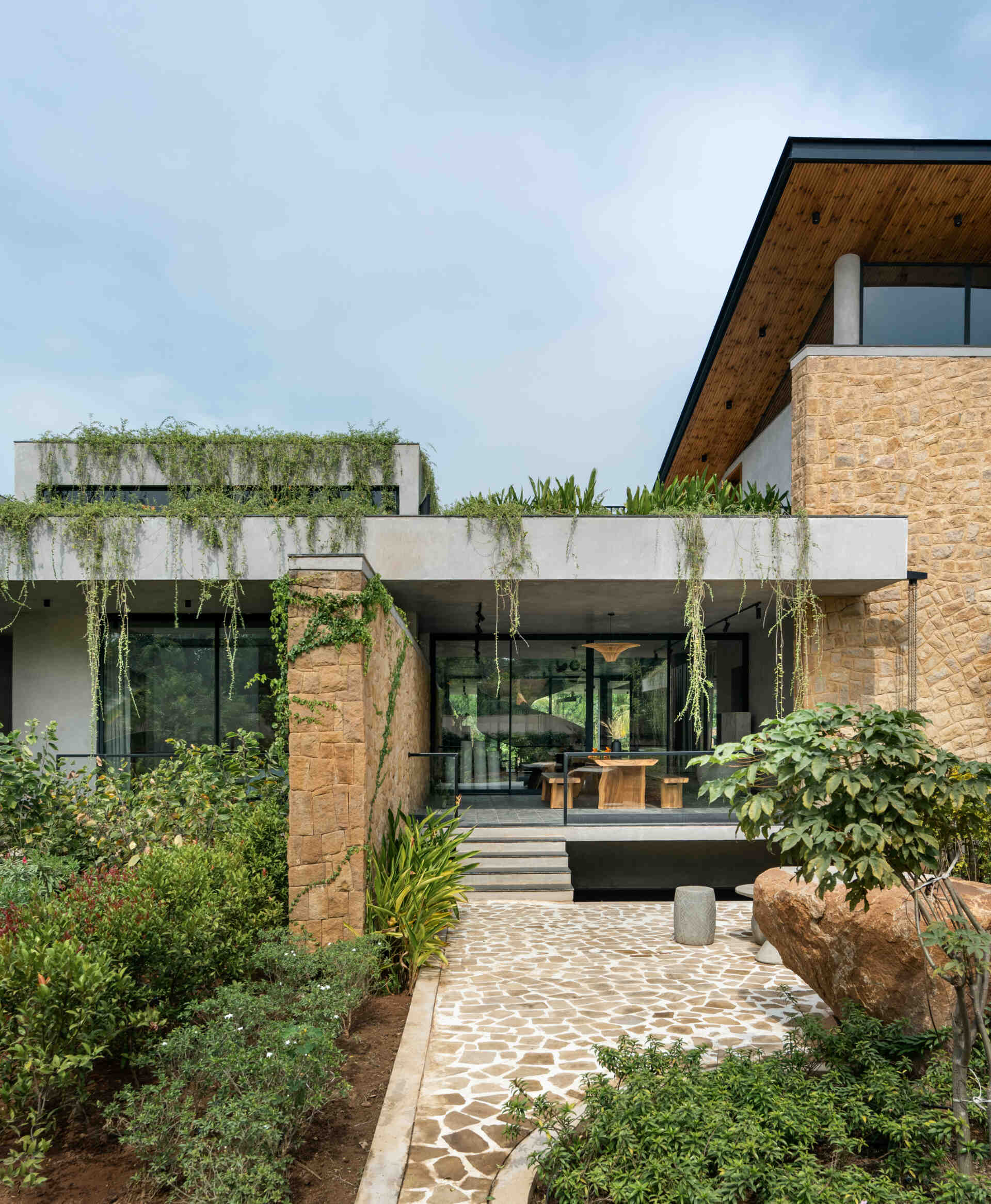 Long stone walls, floating pathways, and deep overhangs shape the architecture and guide movement through the home.