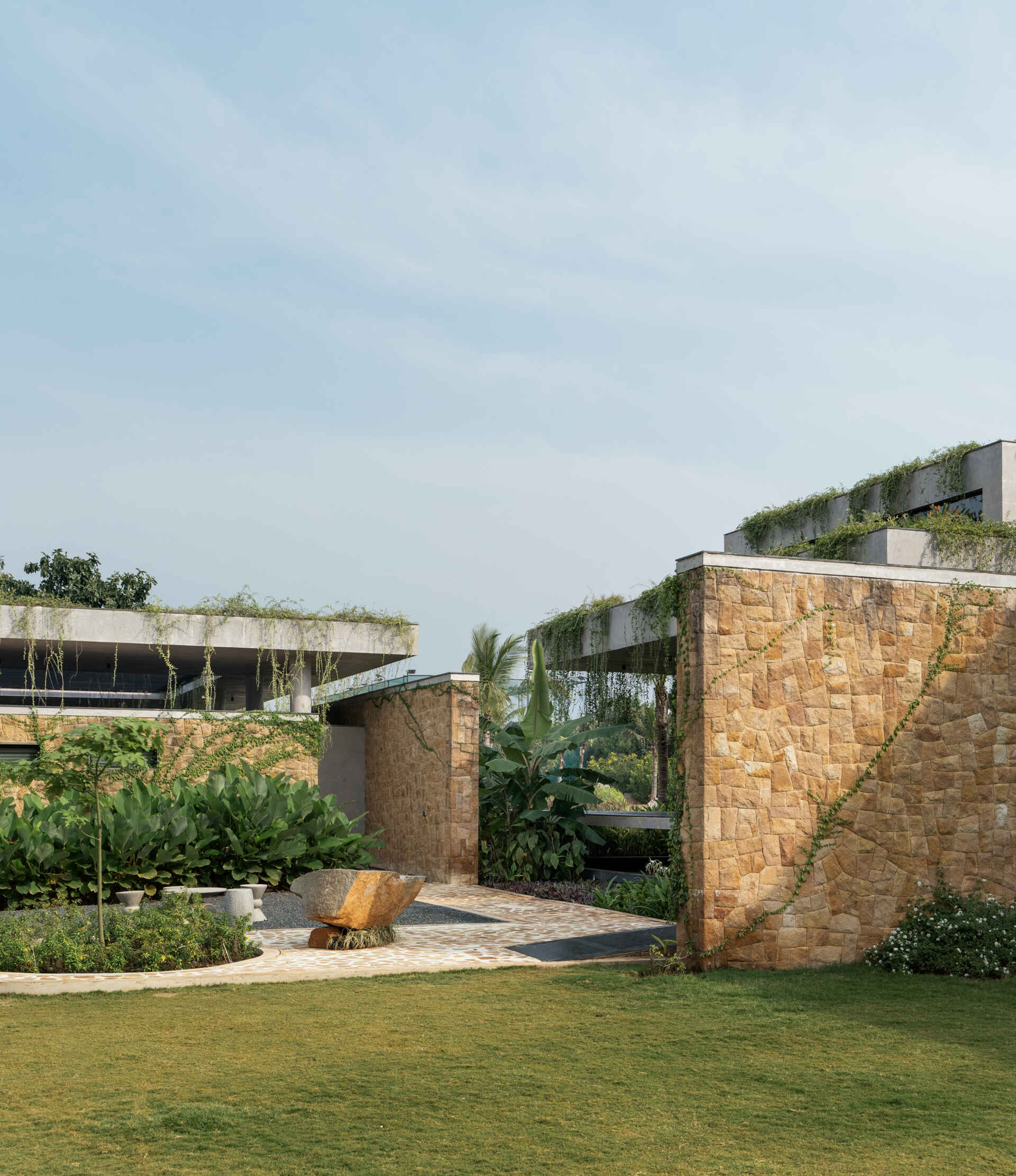 Long stone walls, floating pathways, and deep overhangs shape the architecture and guide movement through the home.