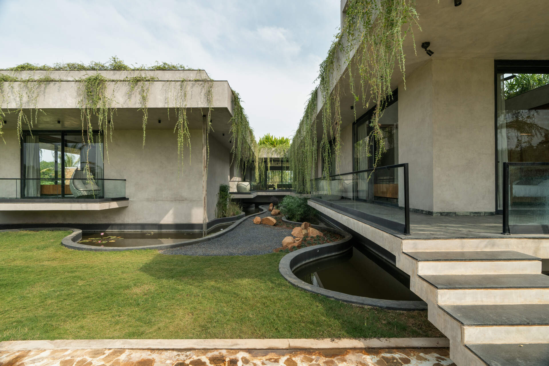 Long stone walls, floating pathways, and deep overhangs shape the architecture and guide movement through the home.