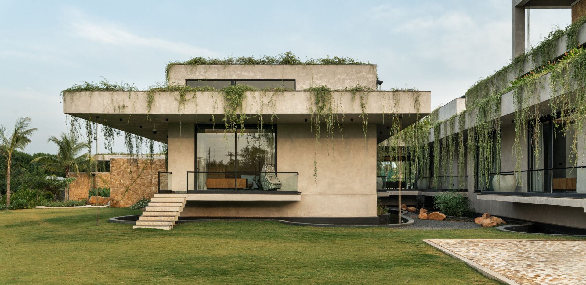 Long stone walls, floating pathways, and deep overhangs shape the architecture and guide movement through the home.