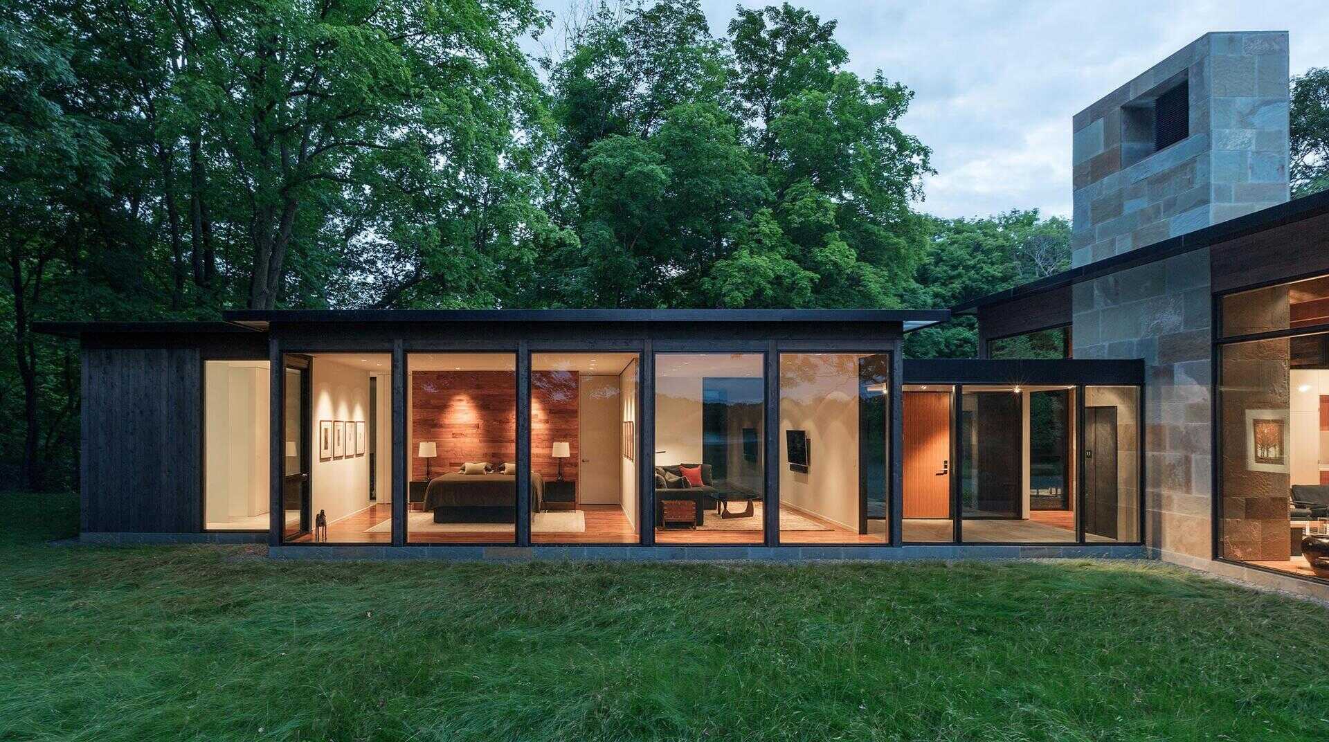 Dark stained cedar, large panes of glass and a bluestone base work together to blend the house into the forest.