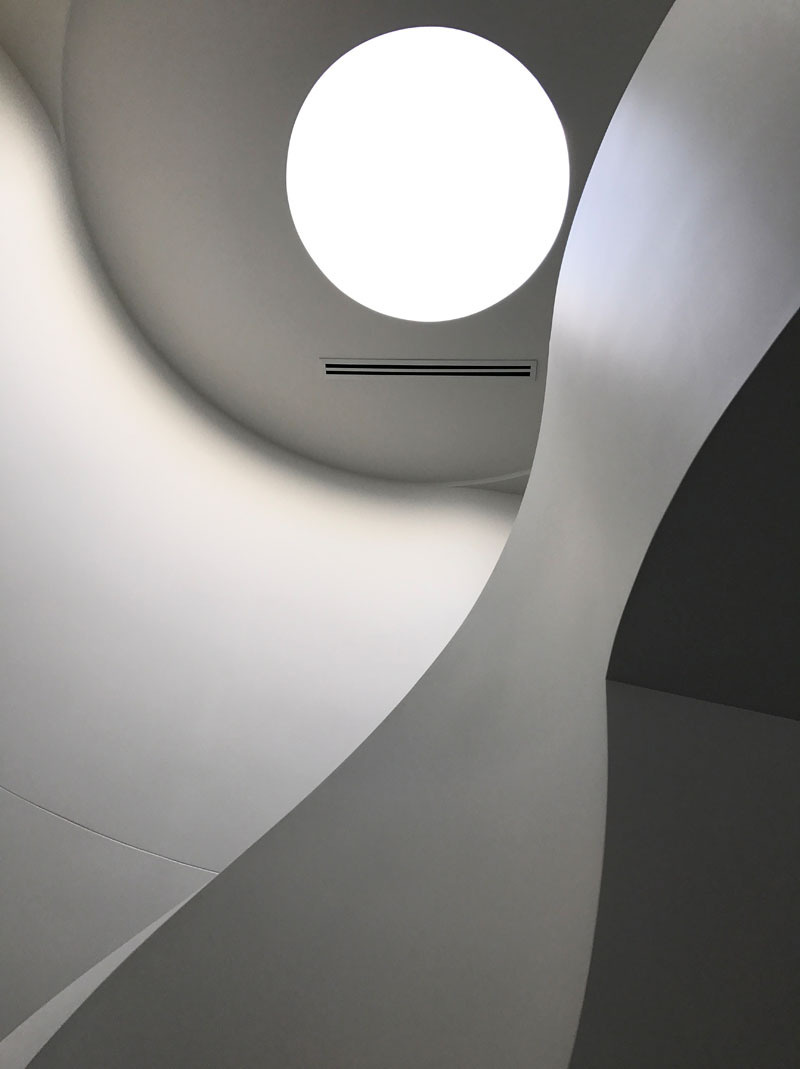 Custom spiral stairs with black treads and a circular skylight above create a sculptural moment inside the home.