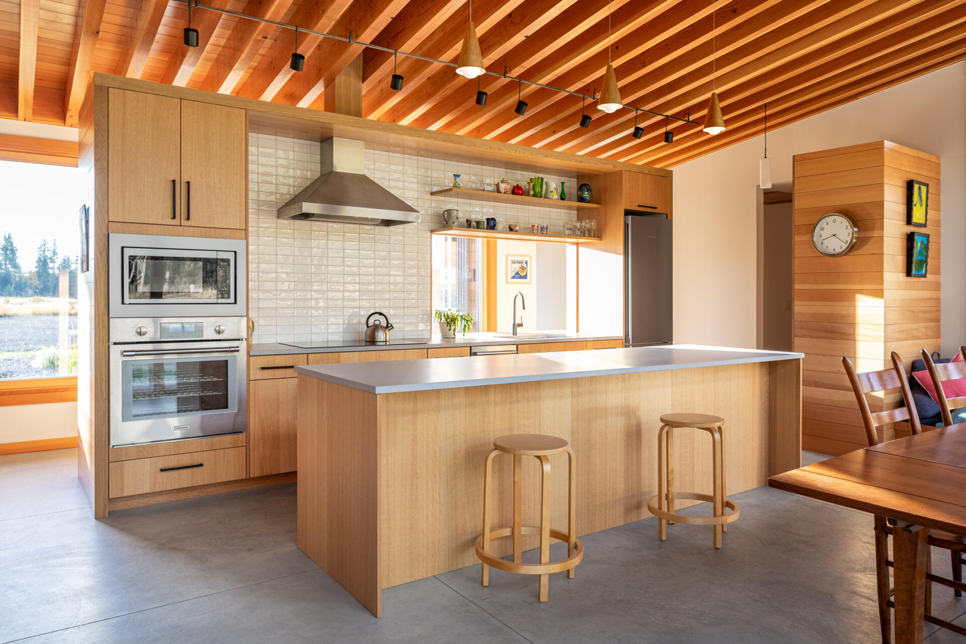 La cocina tiene vistas al prado, haciendo que la naturaleza se sienta parte de la habitación. Un recorte sobre el fregadero brinda visibilidad hacia la entrada, lo que permite a los propietarios ver llegar a los visitantes sin comprometer la sensación de privacidad de la casa.